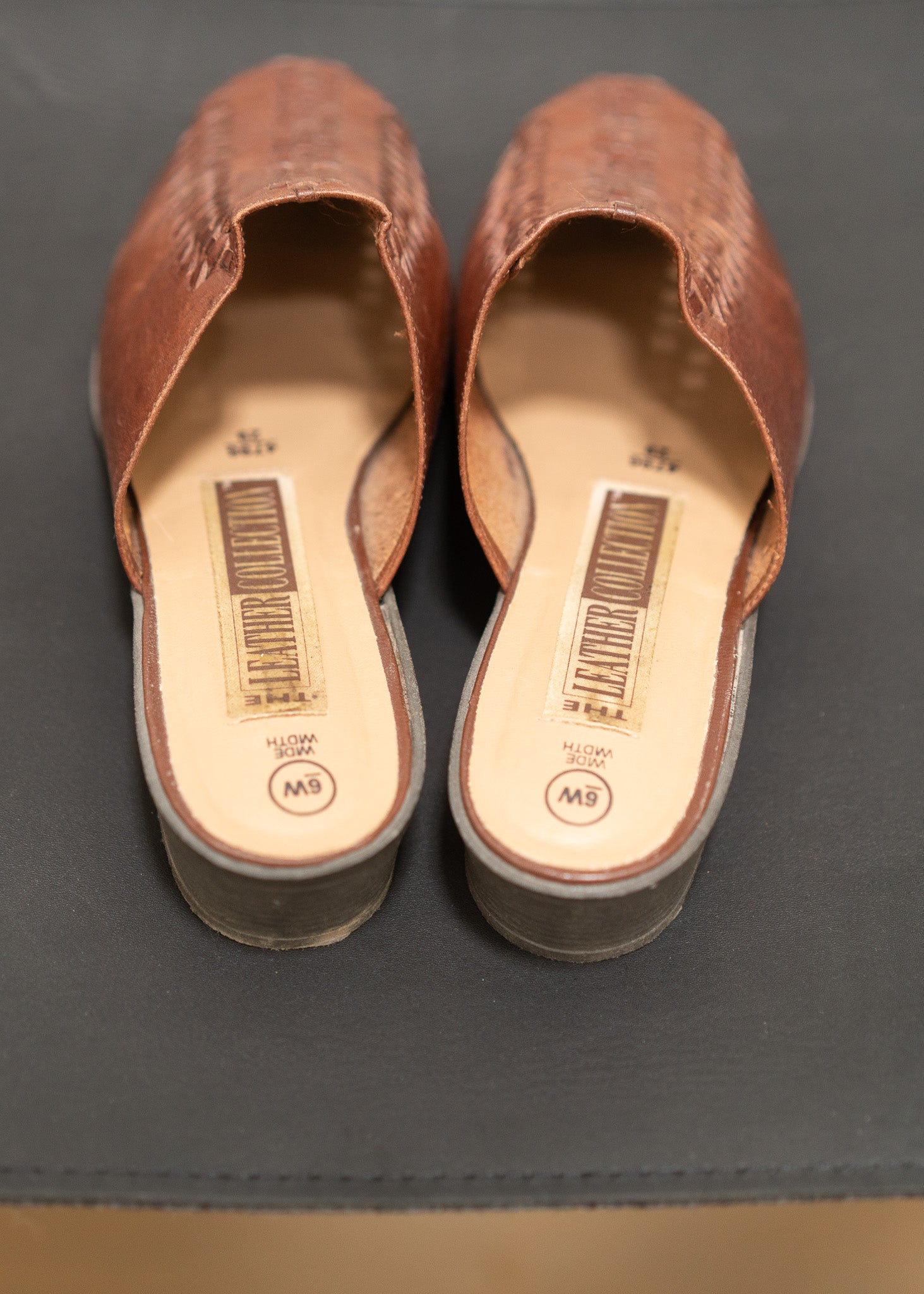 Pair of brown mules with visible brand labels on a gray surface