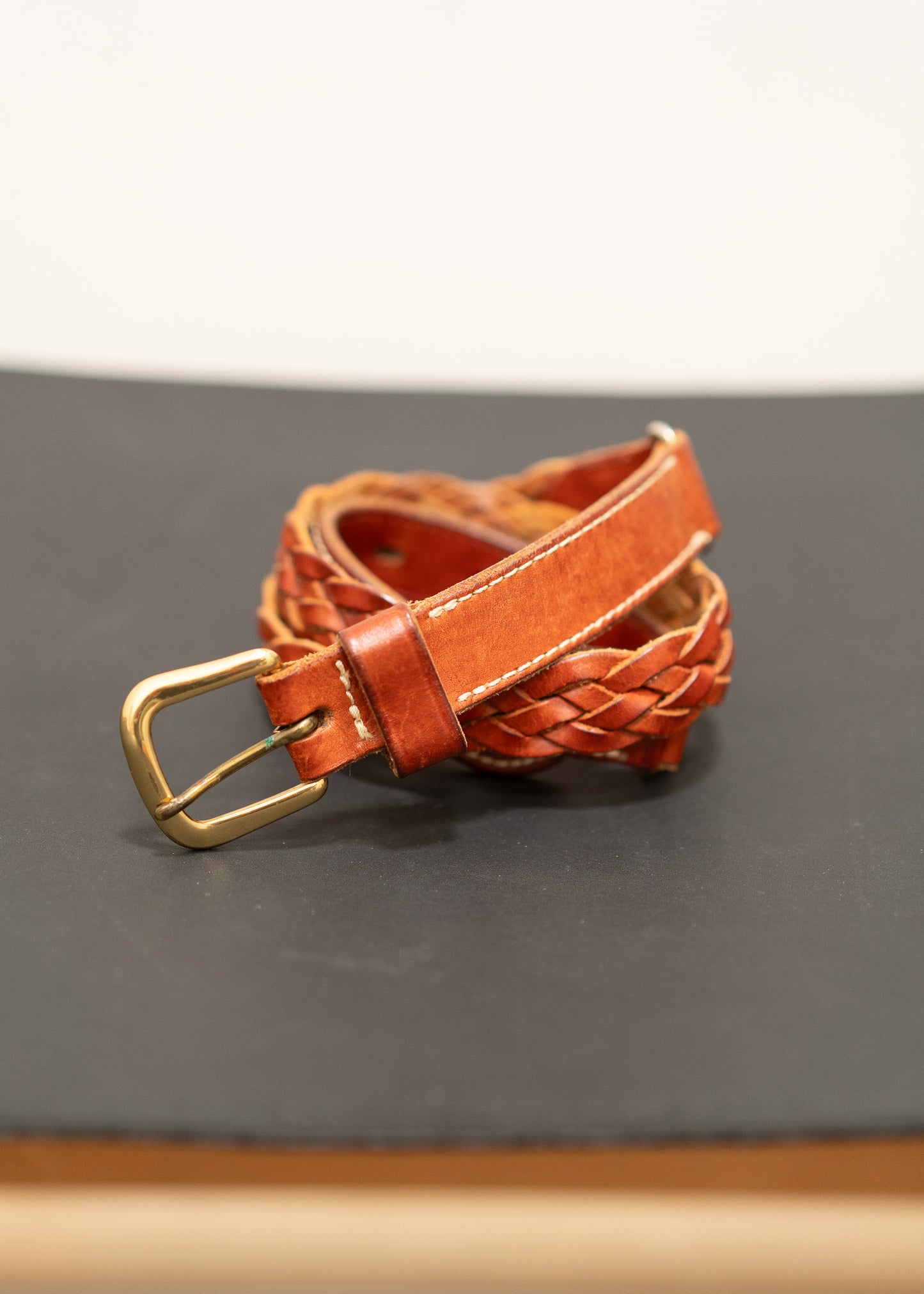 Brown leather belt with a gold brass  buckle on a gray surface