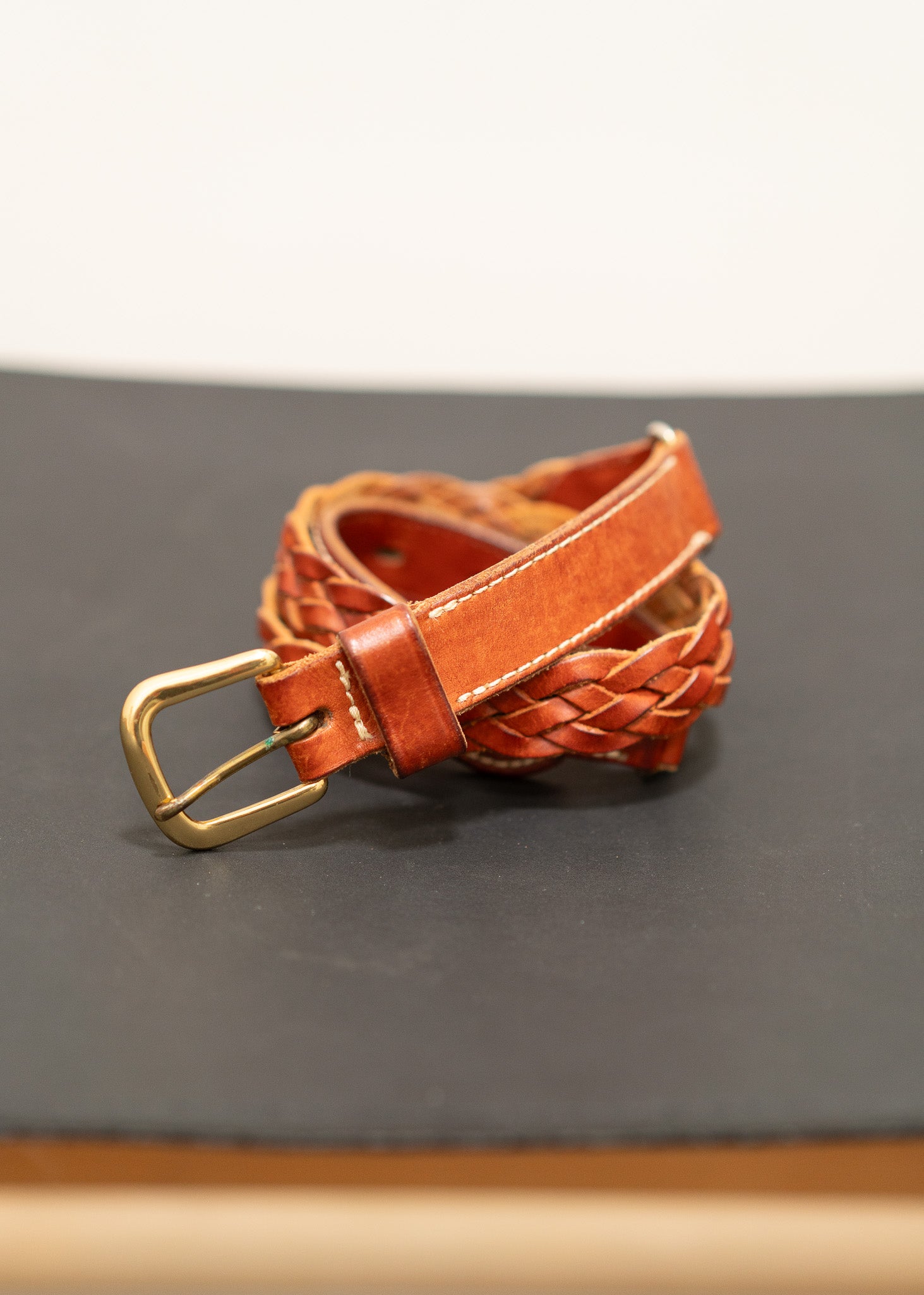 Brown leather belt with a gold brass  buckle on a gray surface
