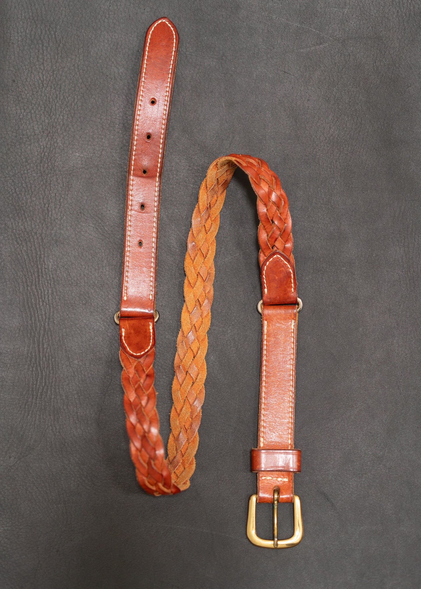 Brown leather belt with braided design on a gray background