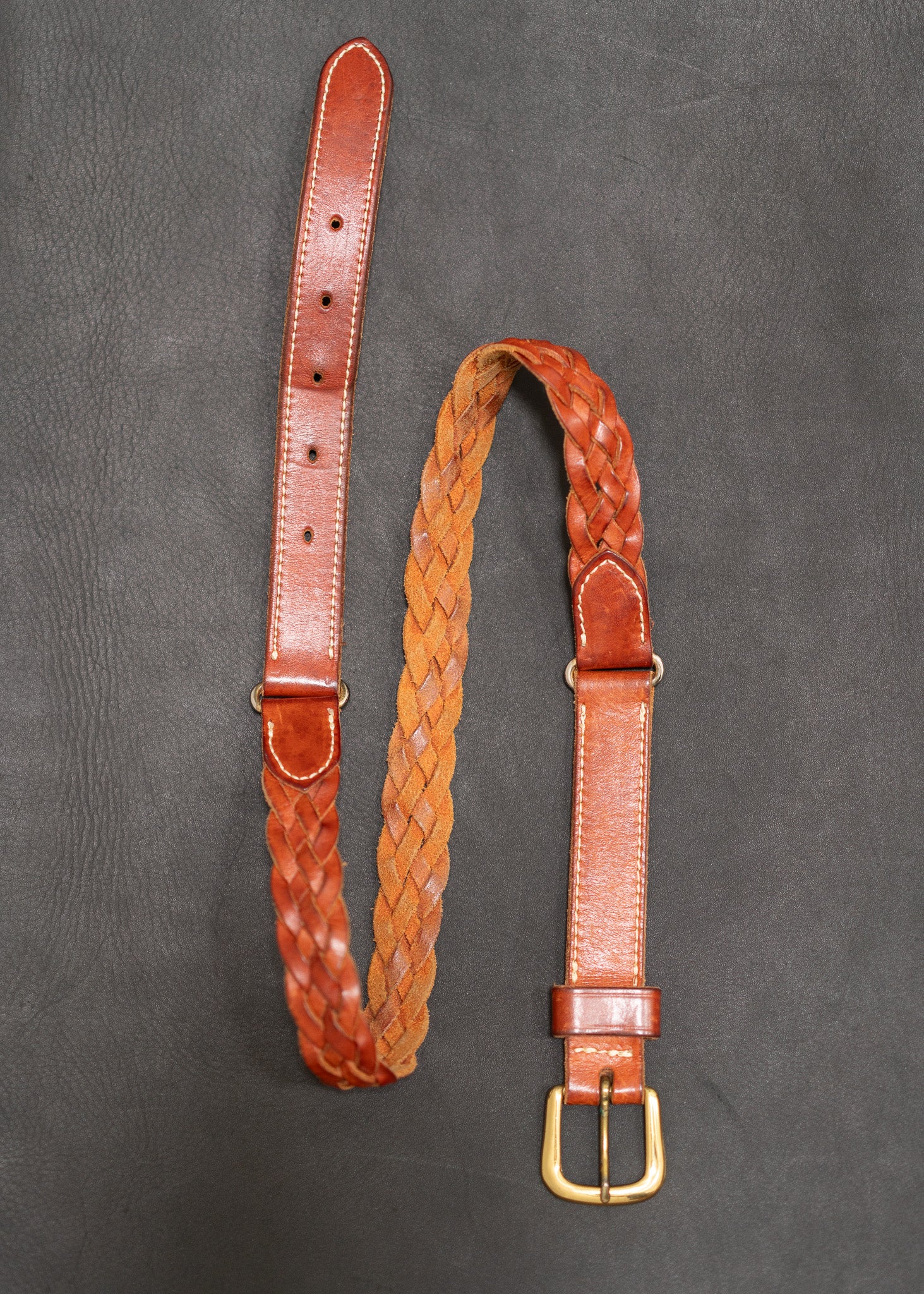 Brown leather belt with braided design on a gray background