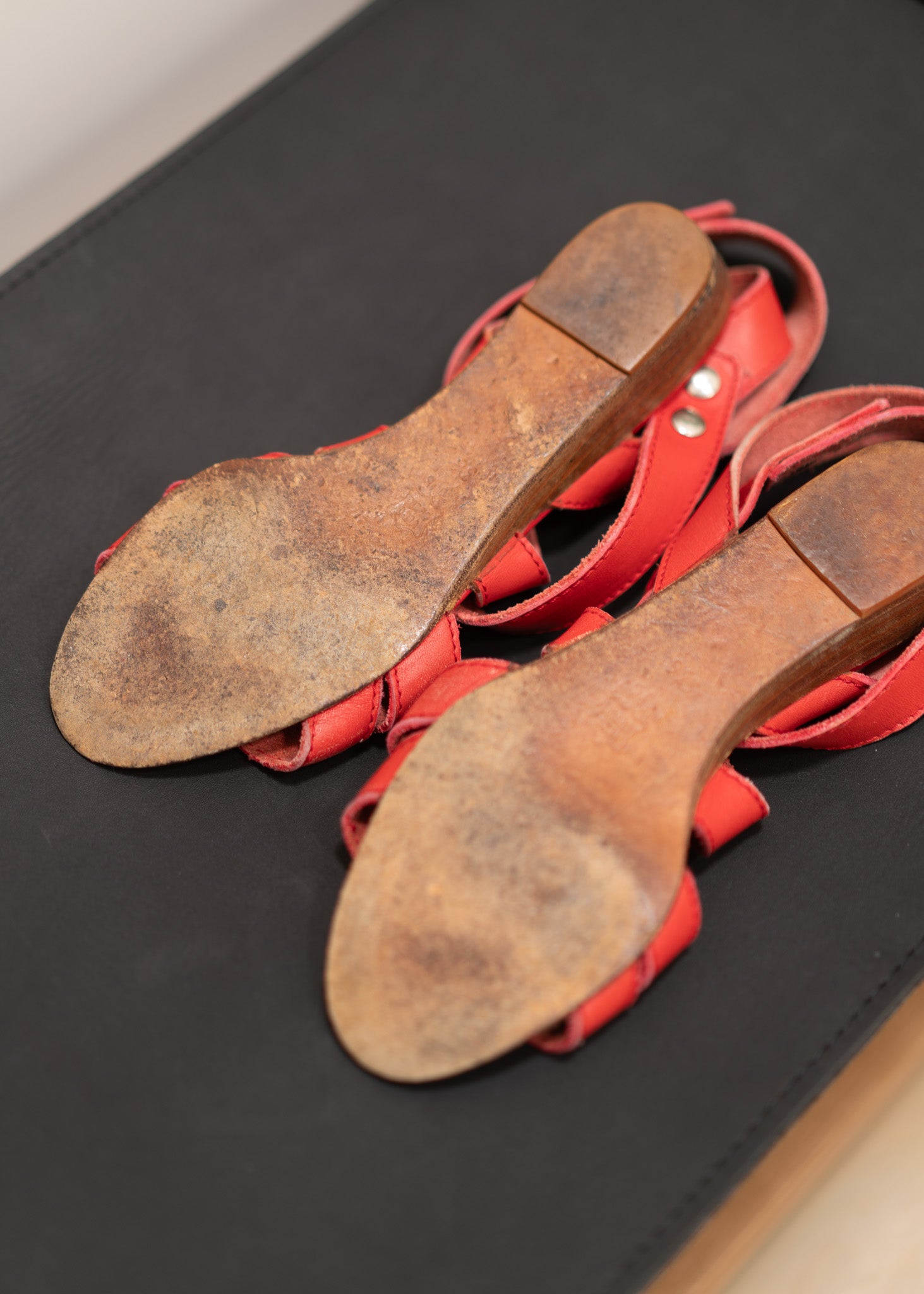 Red sandals with worn soles on a black surface