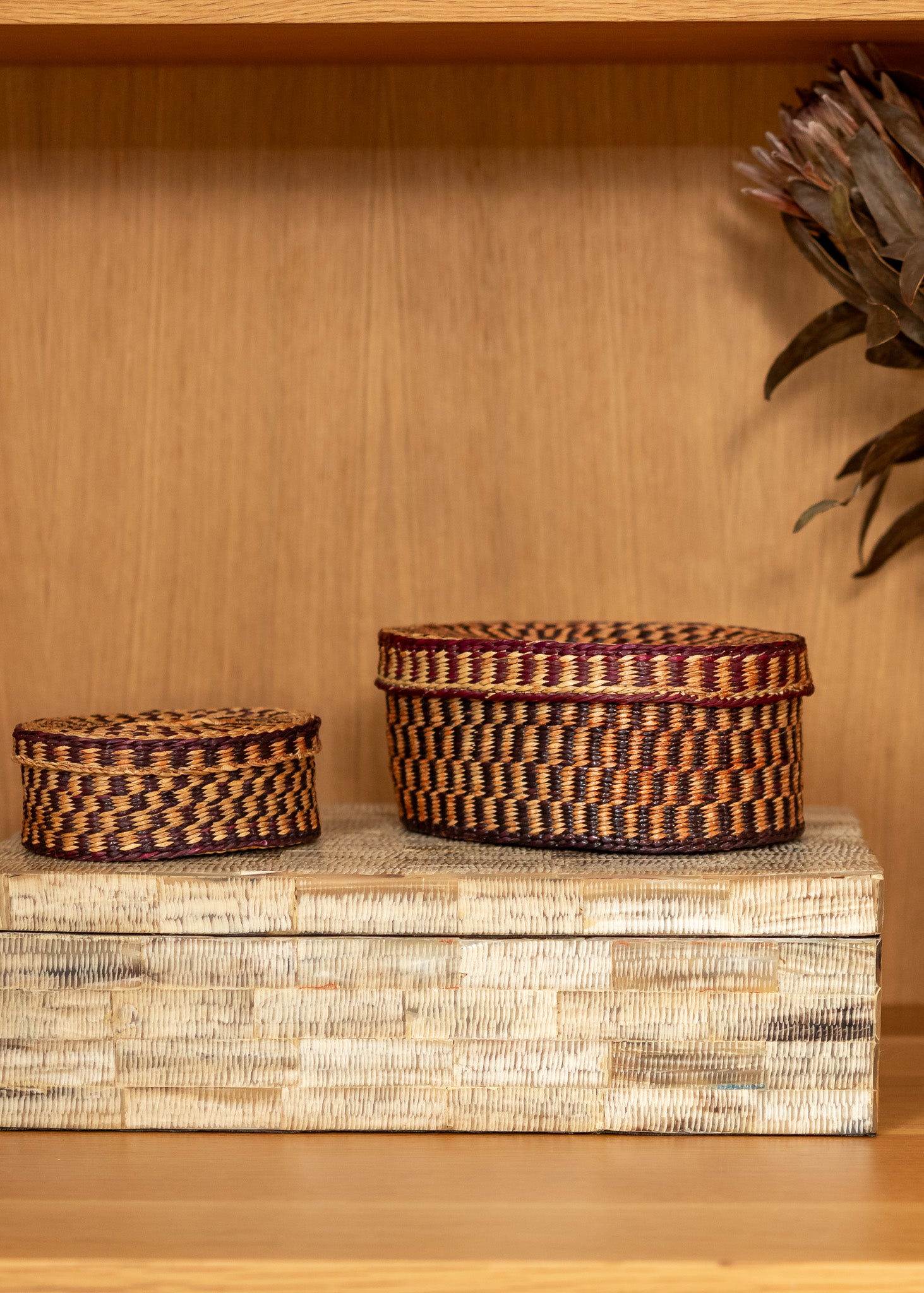 Two vintage woven baskets on a wooden surface with a wooden shelf in the background.