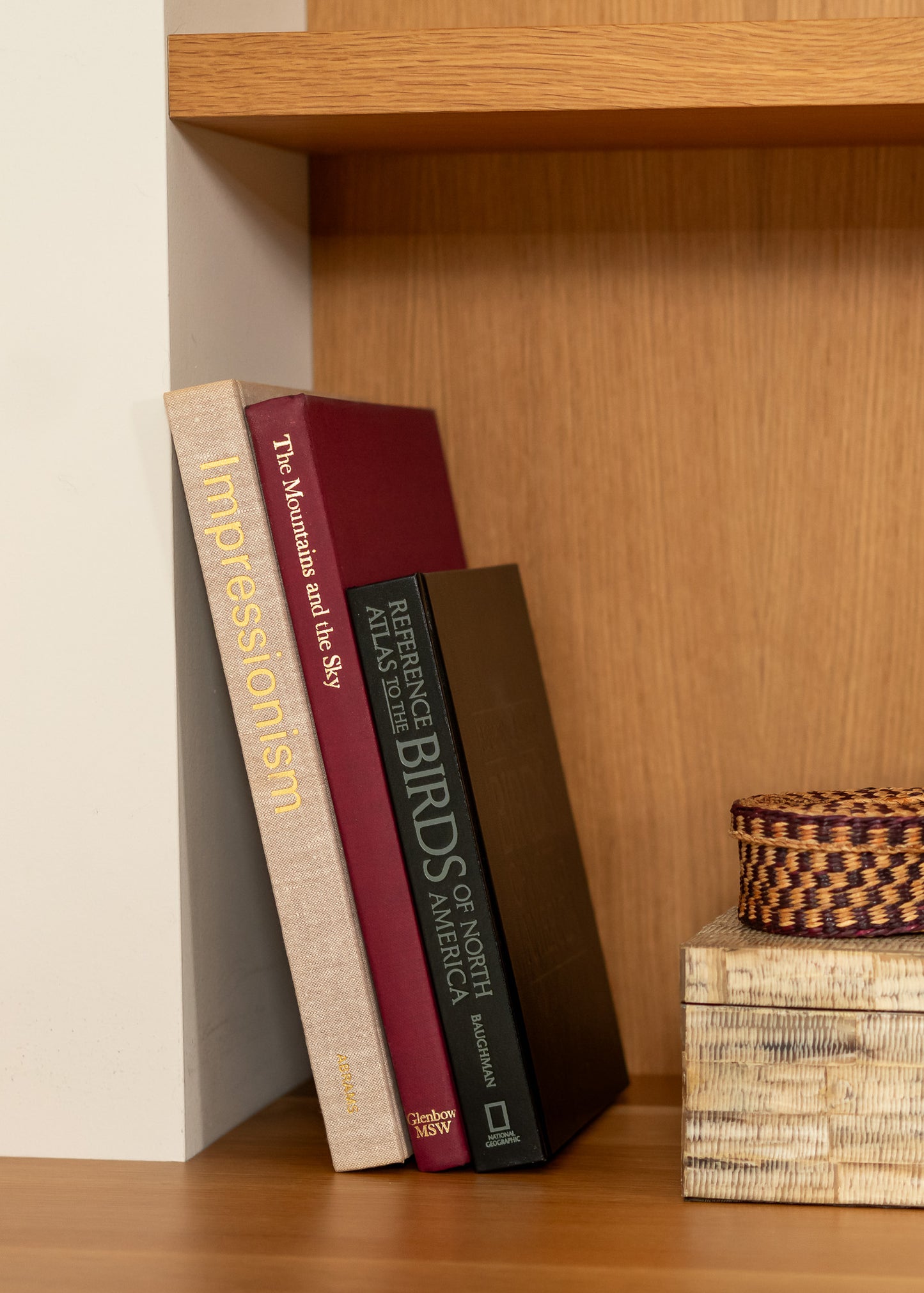 Three vintage books on a wooden shelf with a woven basket on a box.