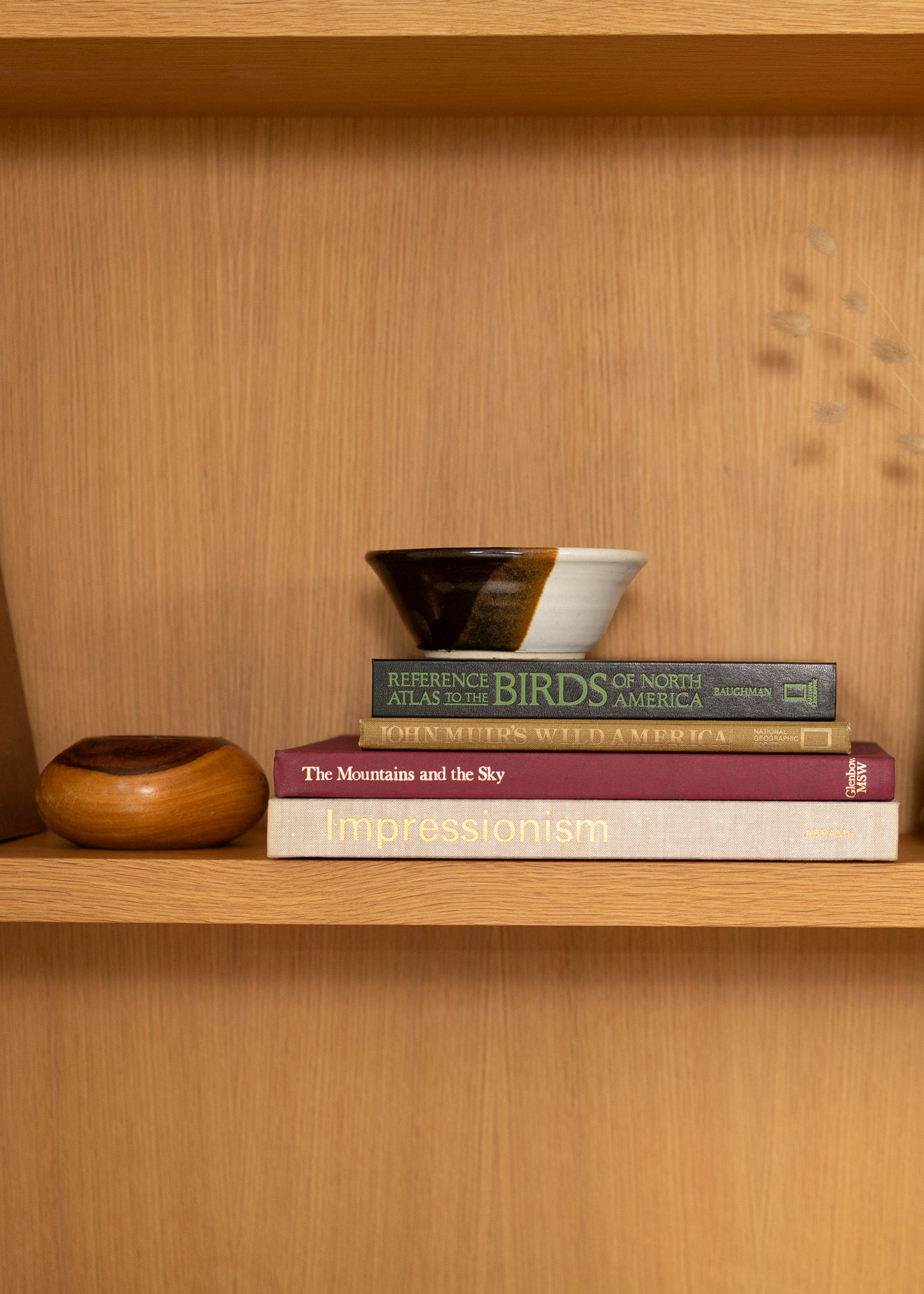 Stack of vintage books on a wooden shelf with decorative bowls.
