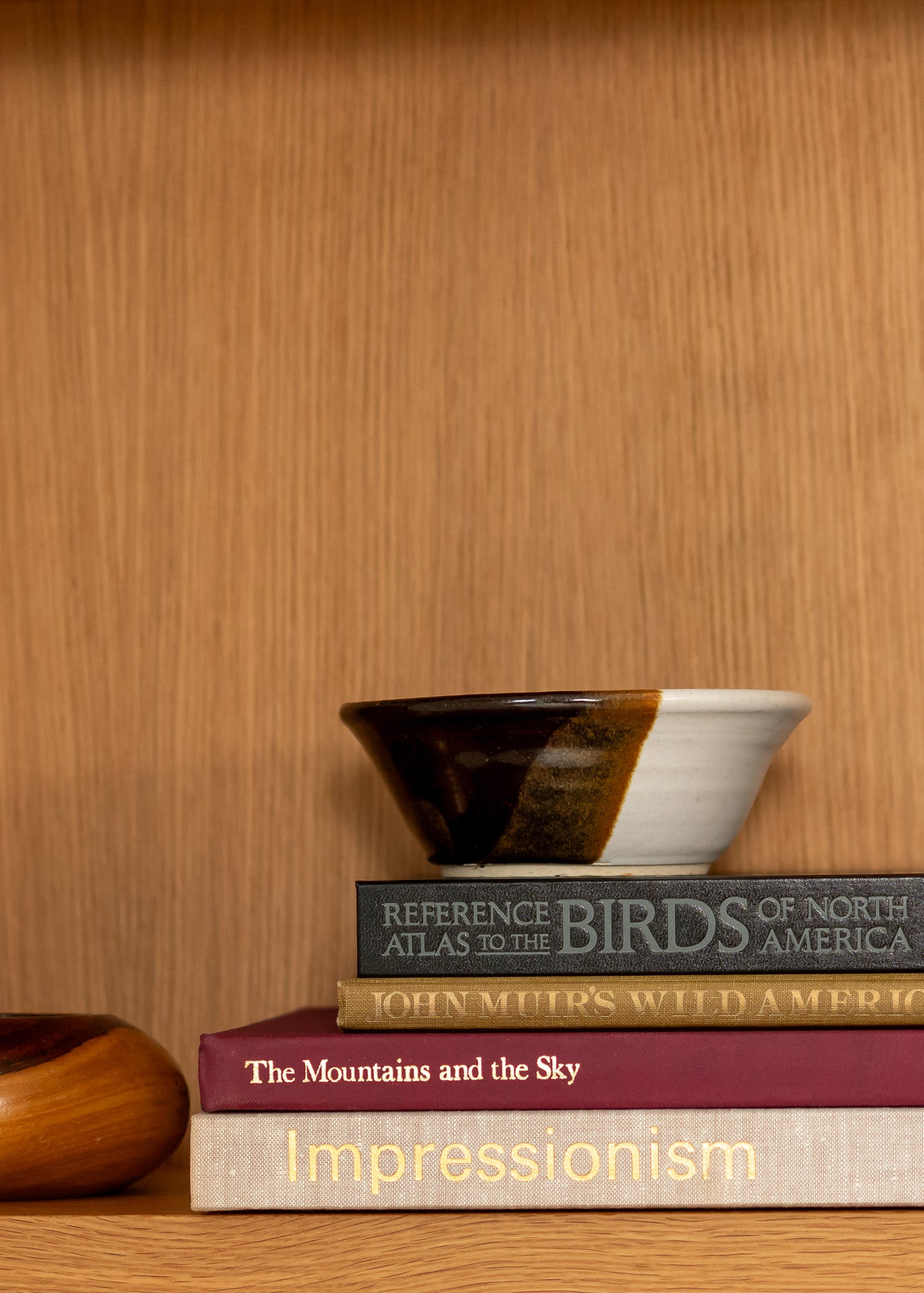 Stack of books on a wooden surface with a vintage ceramic bowl on top