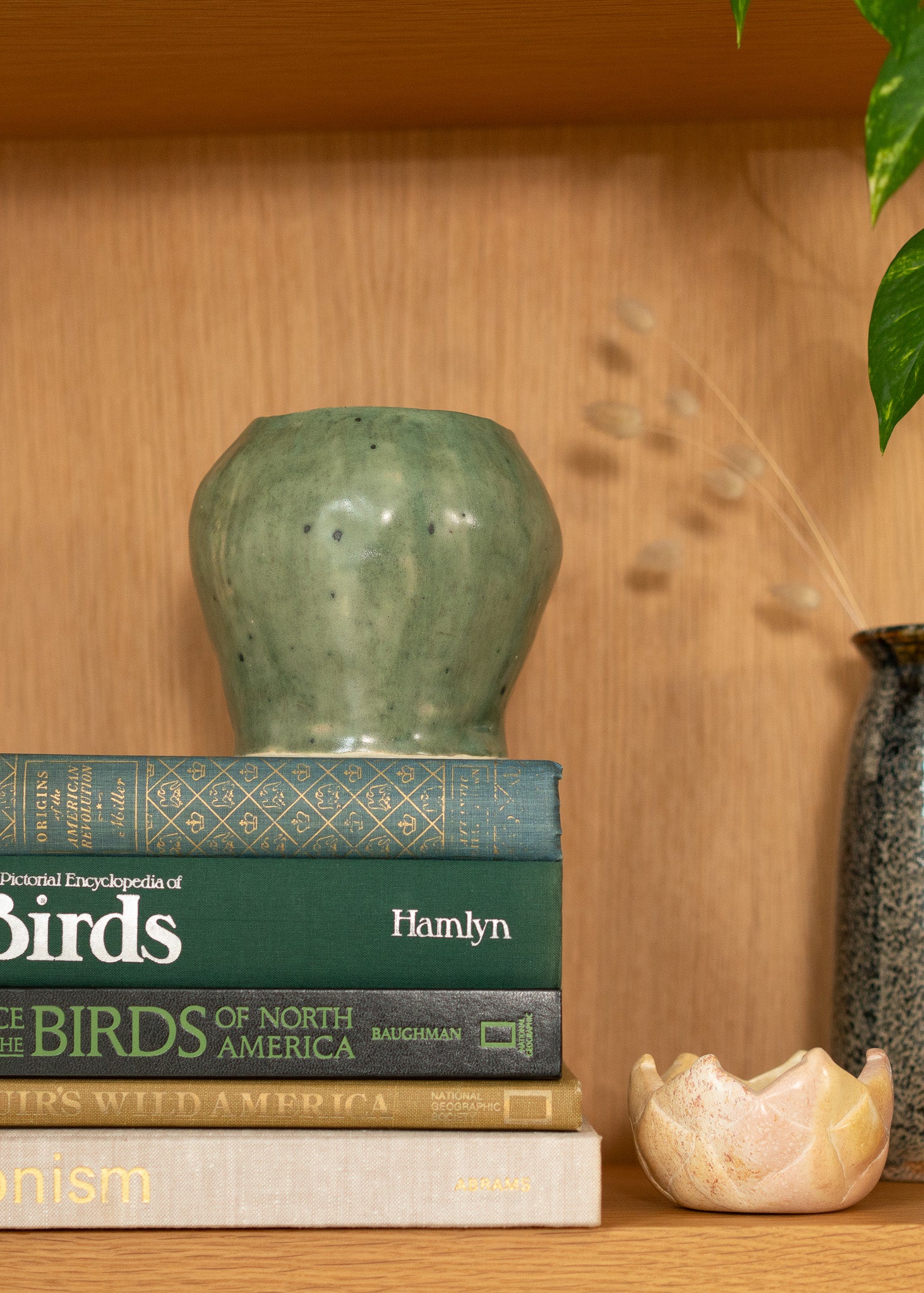 Stack of vintage books on a wooden shelf with a green vase and Small vintage stone bowl 