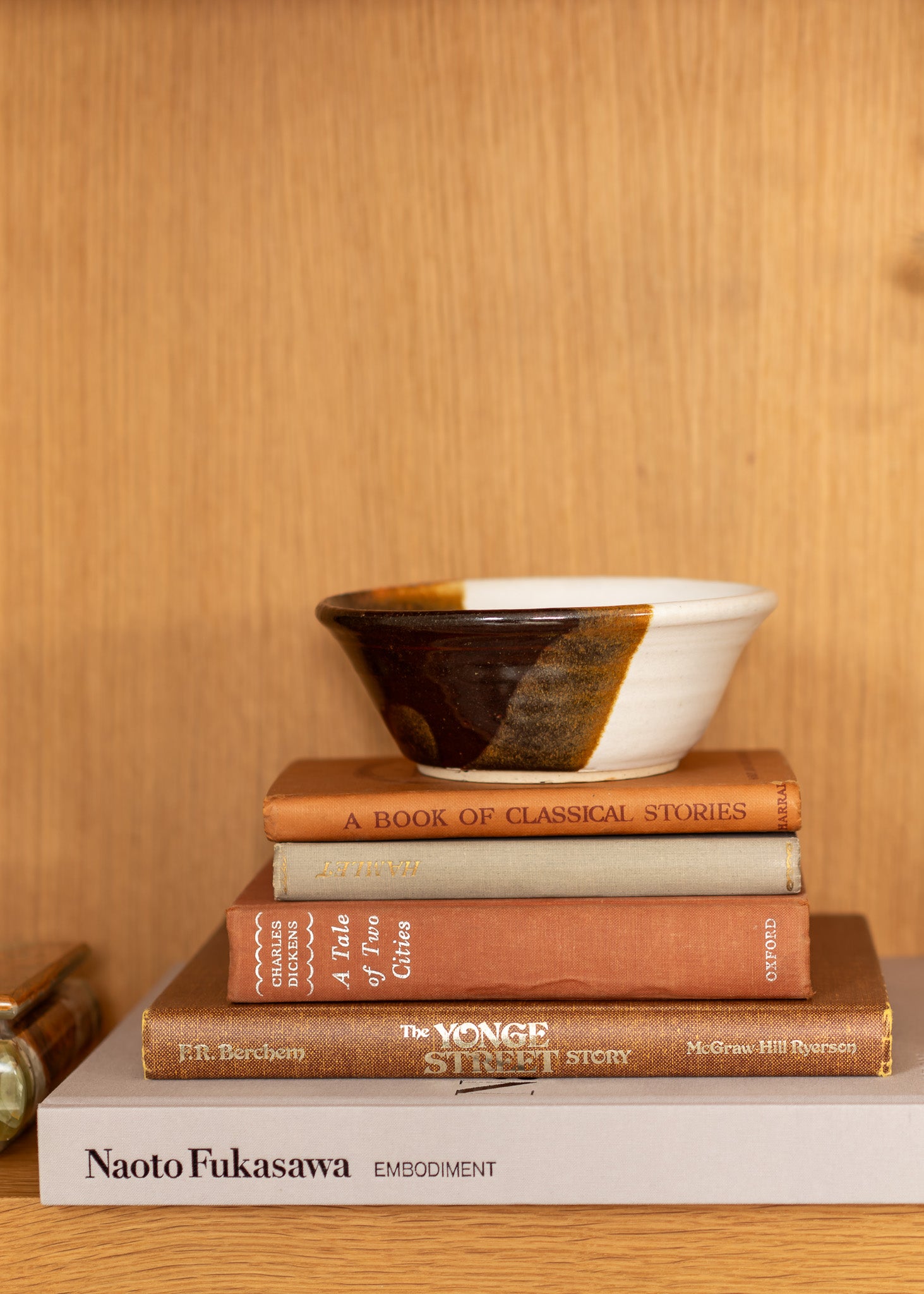 Stack of vintage books with a ceramic bowl on top against a wooden background
