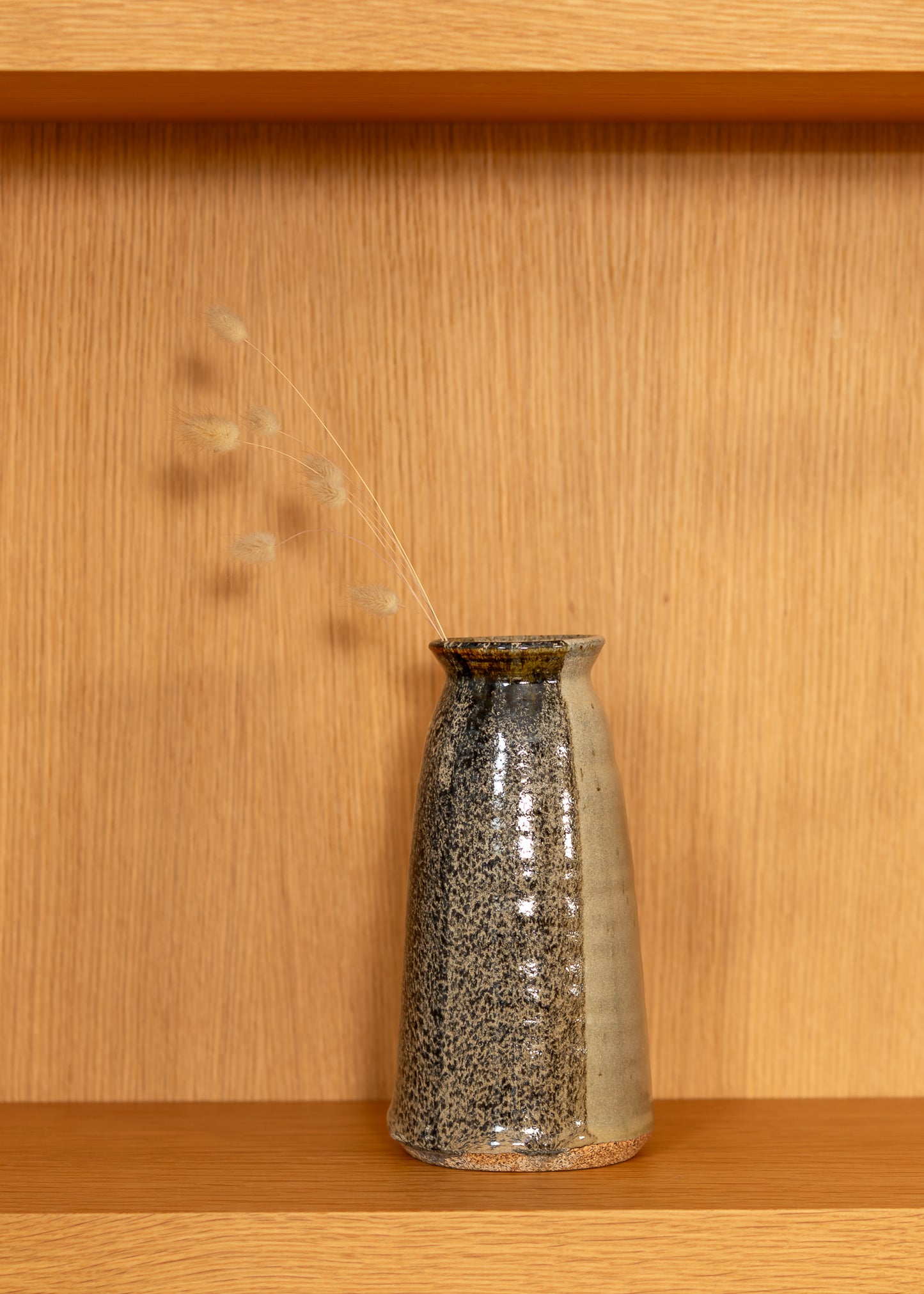Speckled ceramic vase on a wooden shelf with a wooden wall background