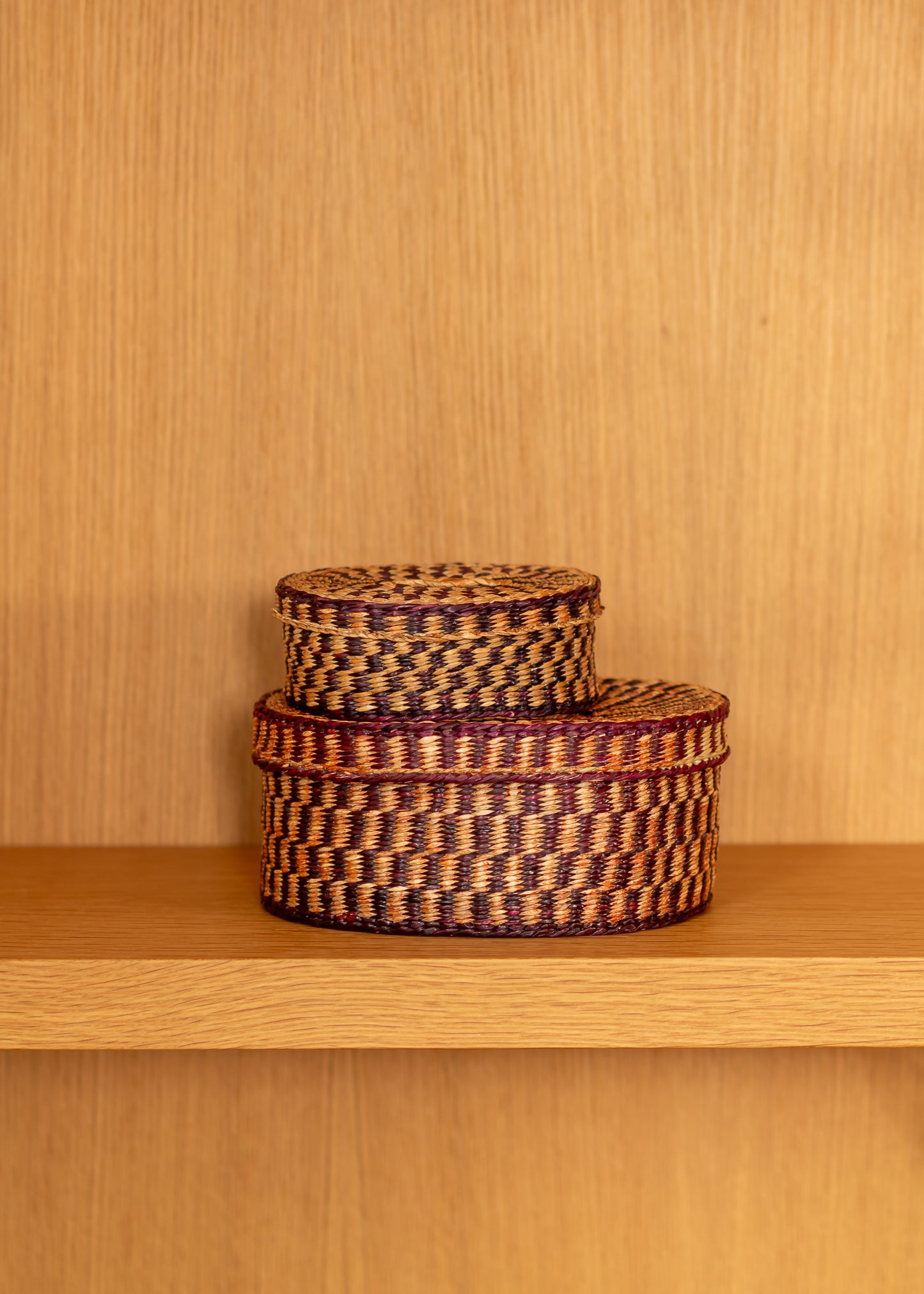 Two vintage woven baskets stacked on a wooden shelf against a wooden wall.