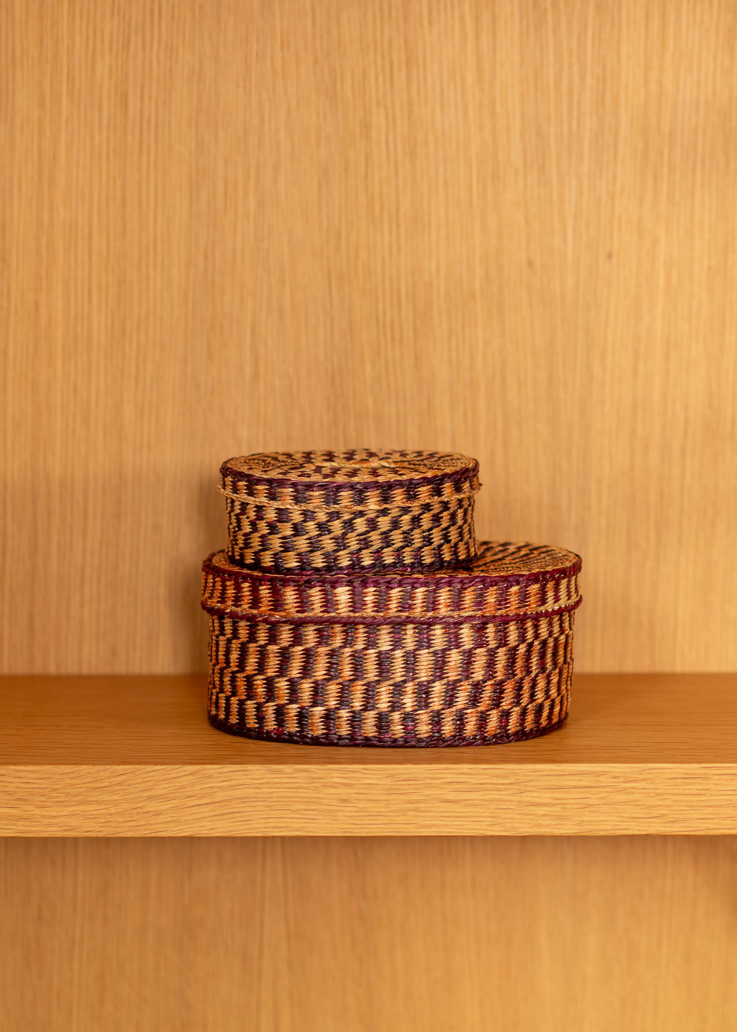 Two vintage woven baskets stacked on a wooden shelf against a wooden wall.