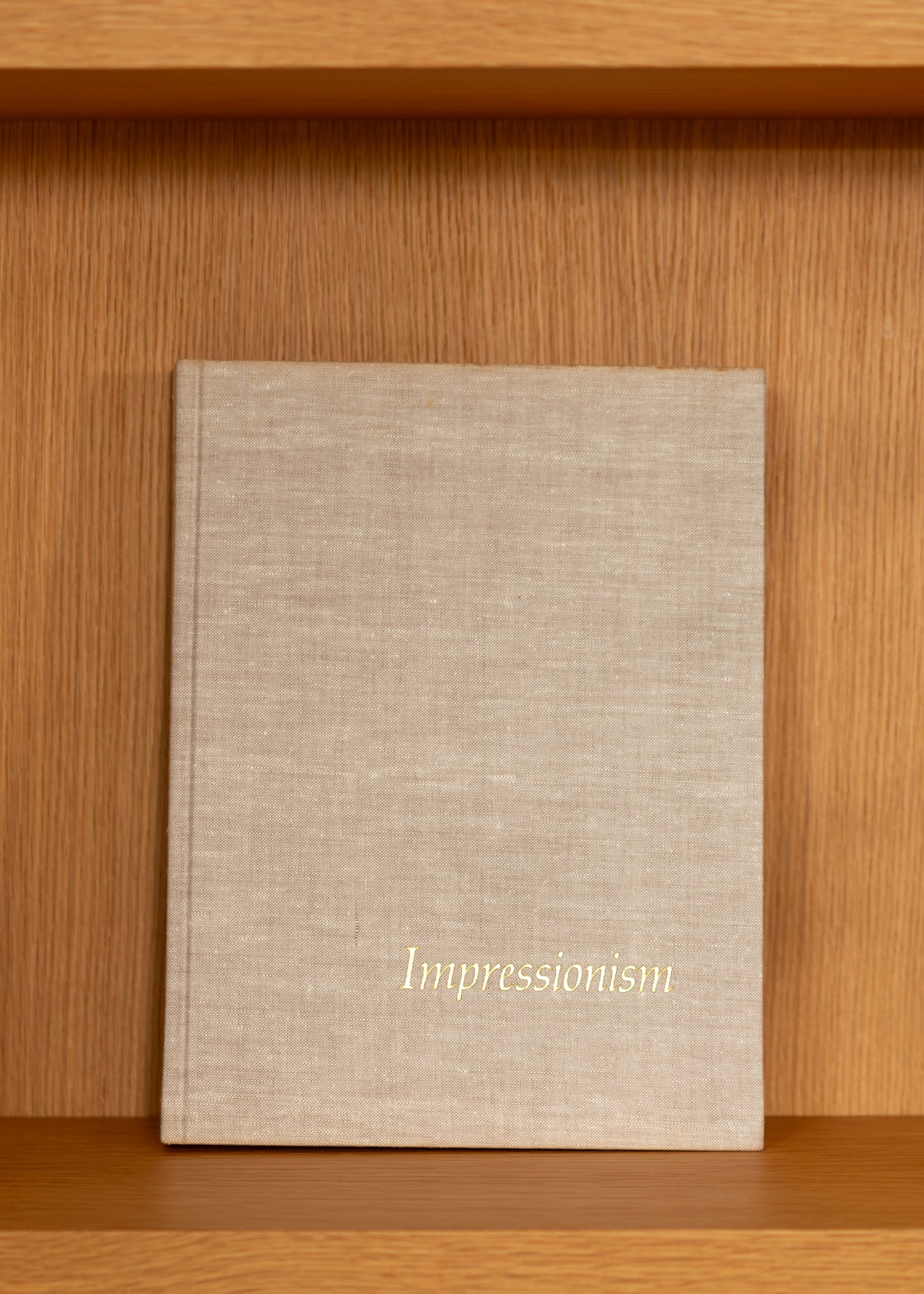 vintage beige linen covered book titled 'Impressionism' on a wooden shelf
