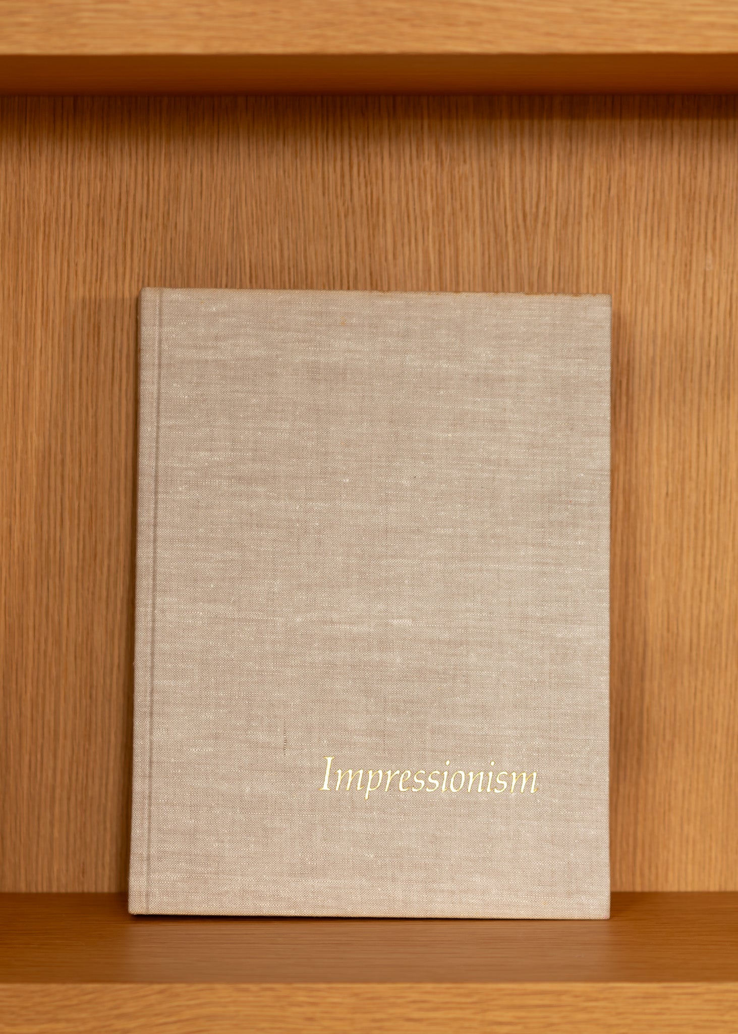 vintage beige linen covered book titled 'Impressionism' on a wooden shelf