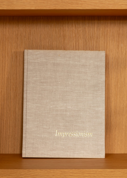vintage beige linen covered book titled 'Impressionism' on a wooden shelf