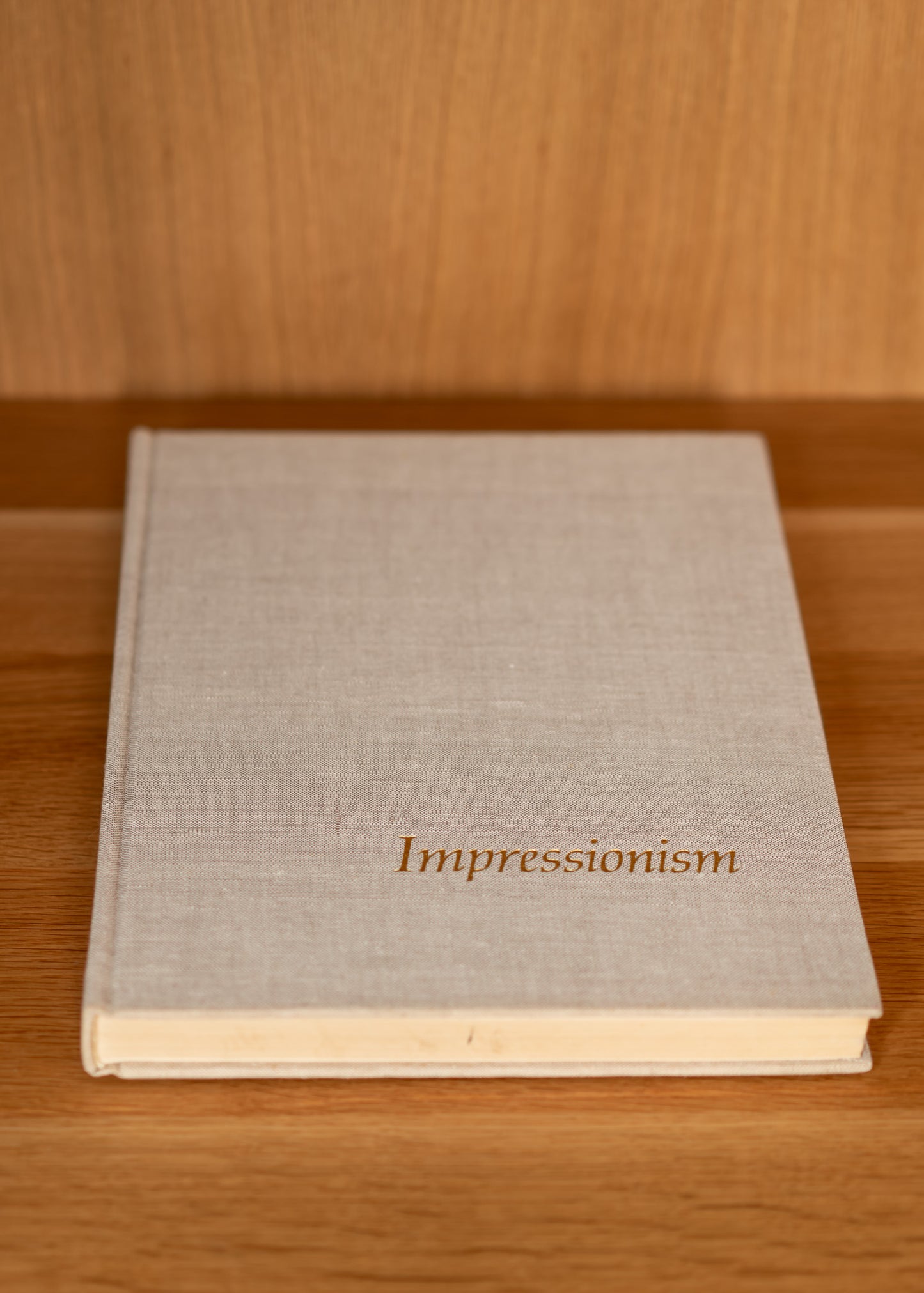 vintage beige linen covered book titled 'Impressionism' on a wooden surface