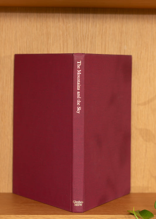Maroon vintage book with 'The Mountains and the Sky' title on a wooden surface