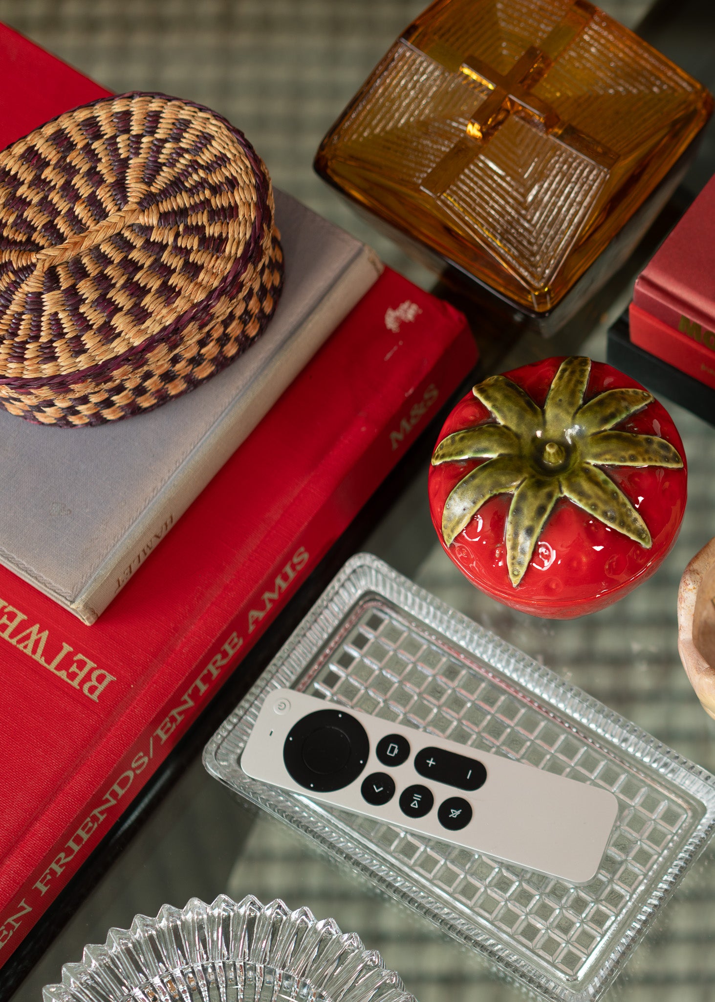 Collection of vintage decorative items including a woven basket, books, a tomato figurine, and a remote control on a textured surface.