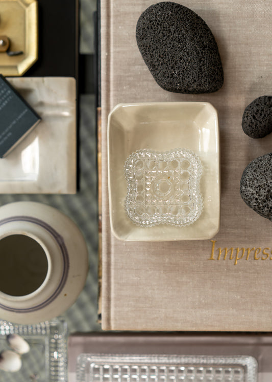 Table setting with a square vintage glass dish, ceramic bowl, and decorative stones on a textured surface.