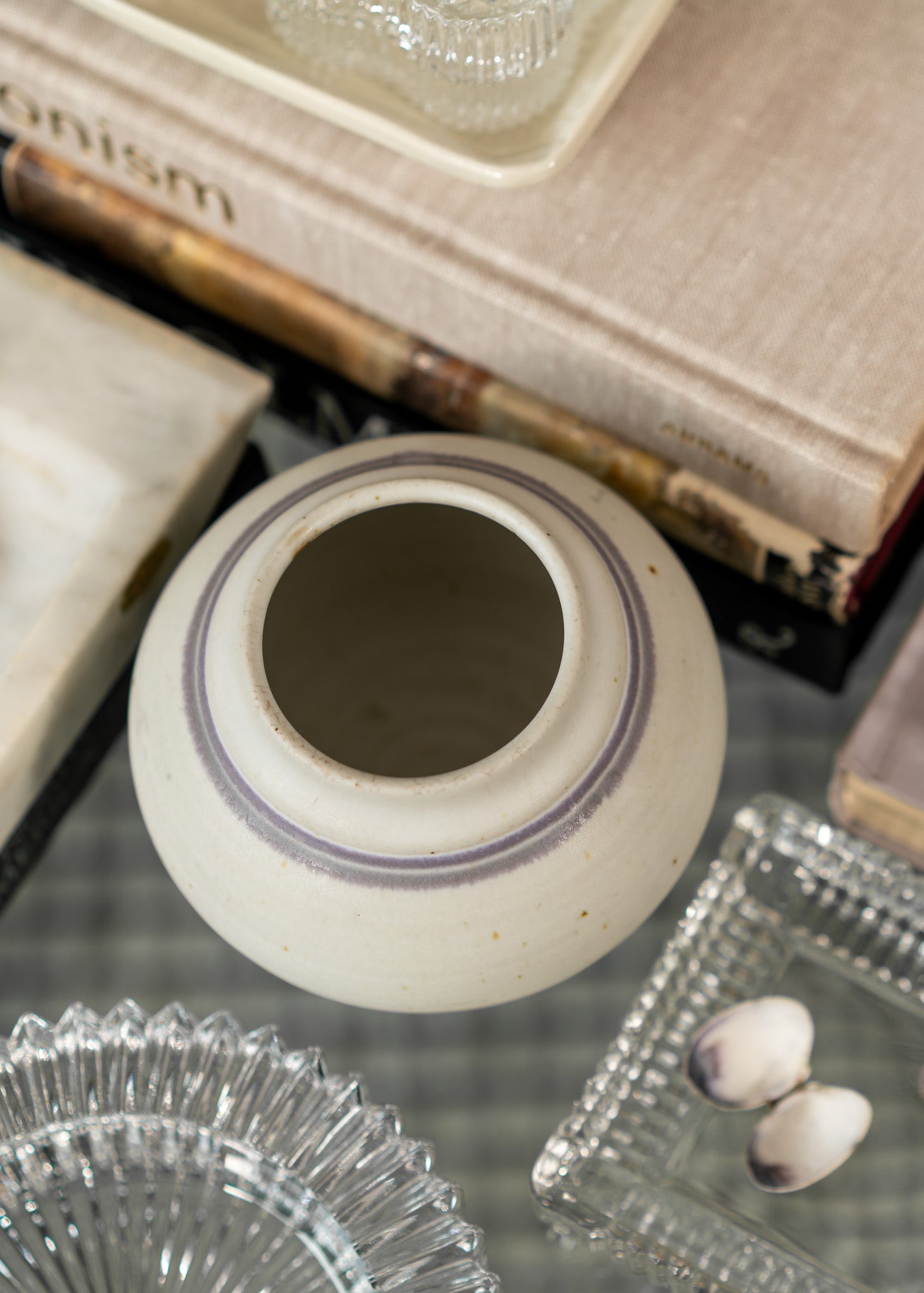 Vintage white ceramic pot with purple rim on a glass surface with books and glassware in the background