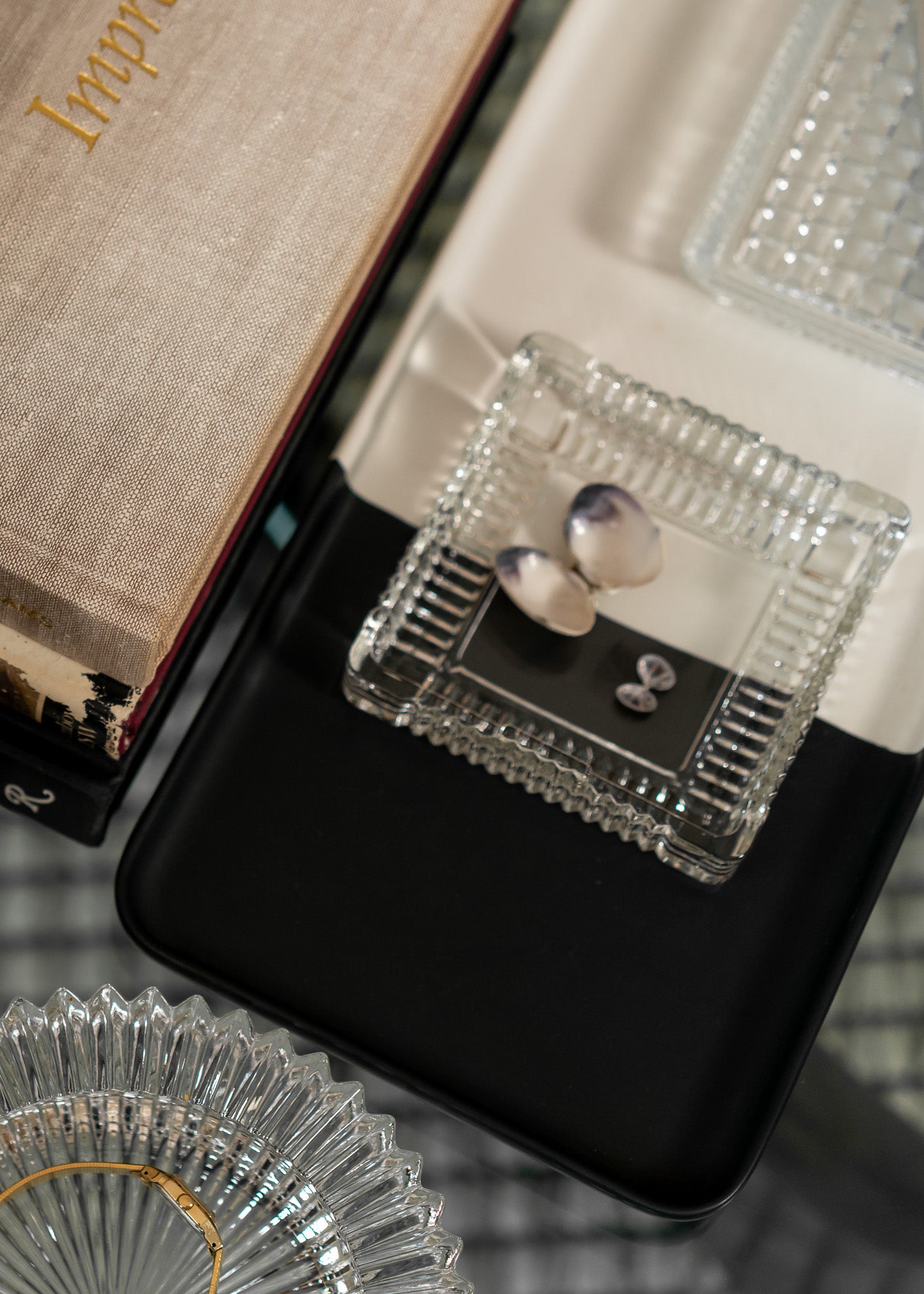 Close-up of a vintage clear glass jewelry box with a black lid on a textured surface.