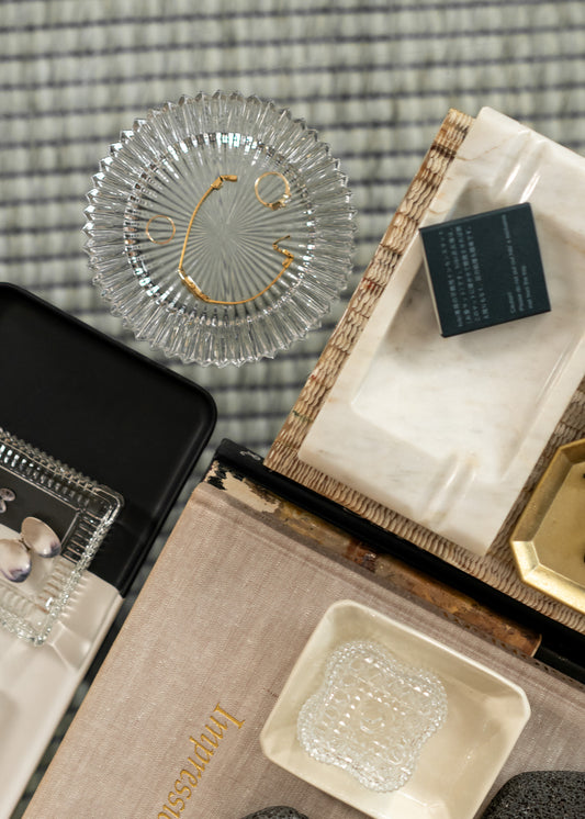 Collection of decorative items including a vintage glass dish, small box, and crystal object on a checkered fabric background.