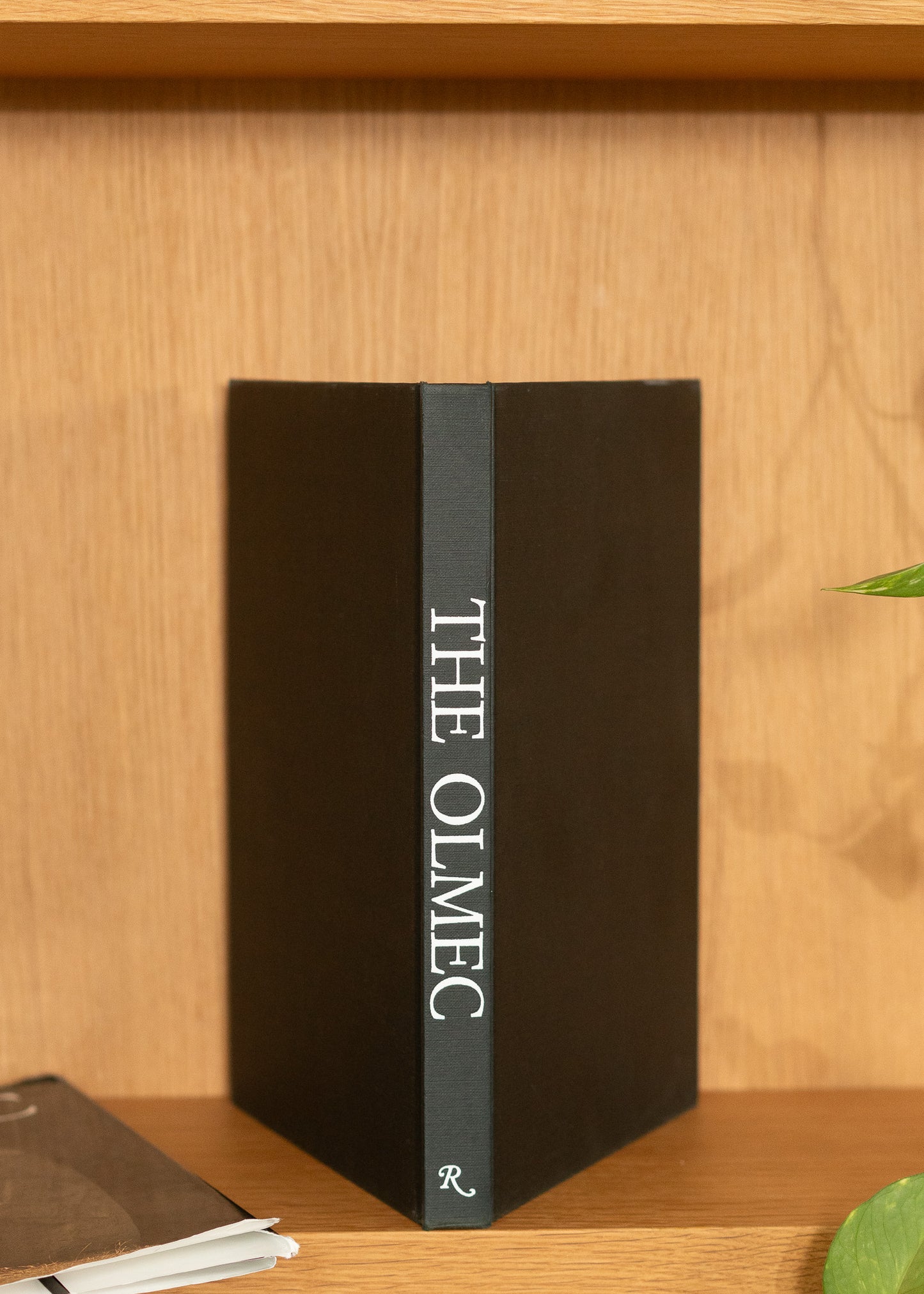 Vintage black book titled 'The Olmec' on a wooden shelf