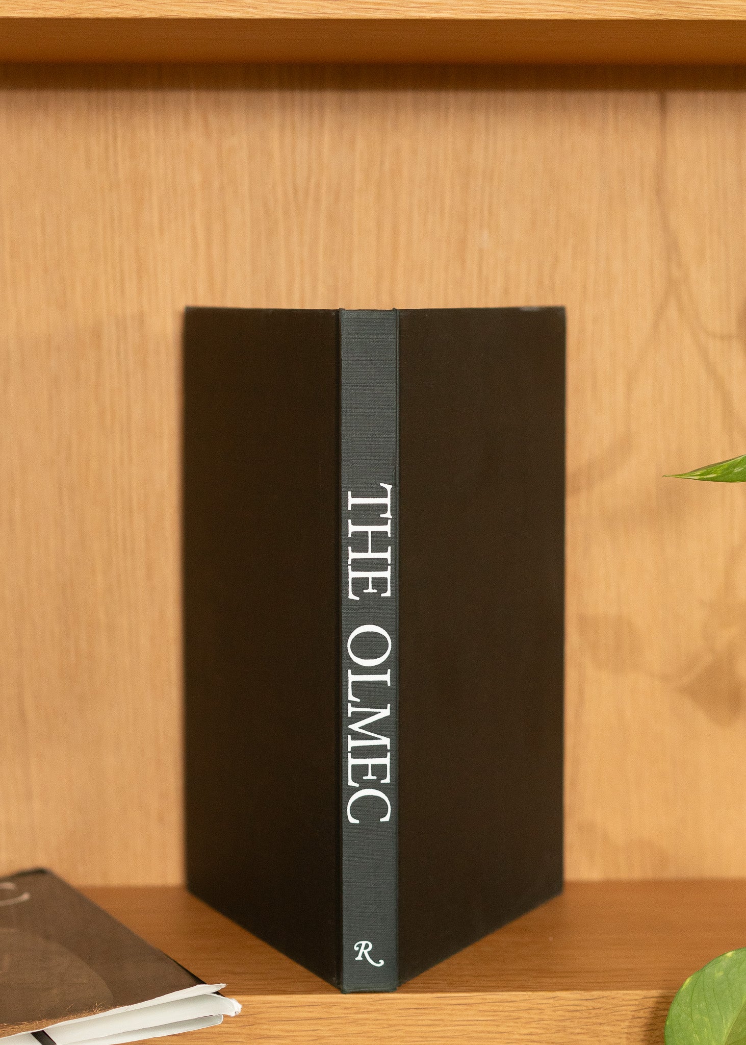 Vintage black book titled 'The Olmec' on a wooden shelf