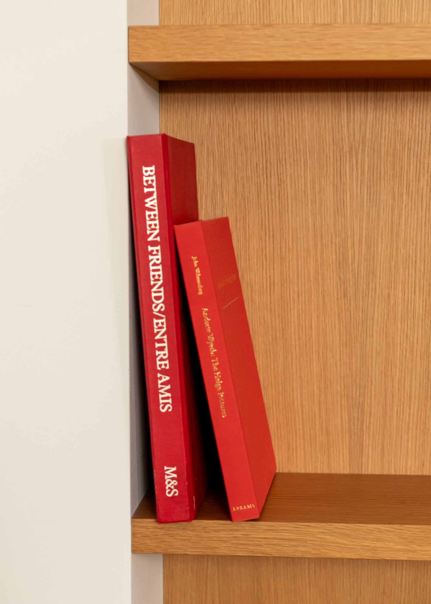 Two vintage red books titled 'Entre Amis' on a wooden shelf.
