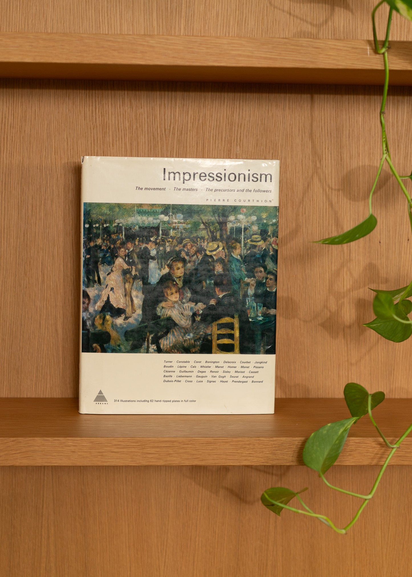 Vintage book titled 'Impressionism' on a wooden shelf with a plant in the background