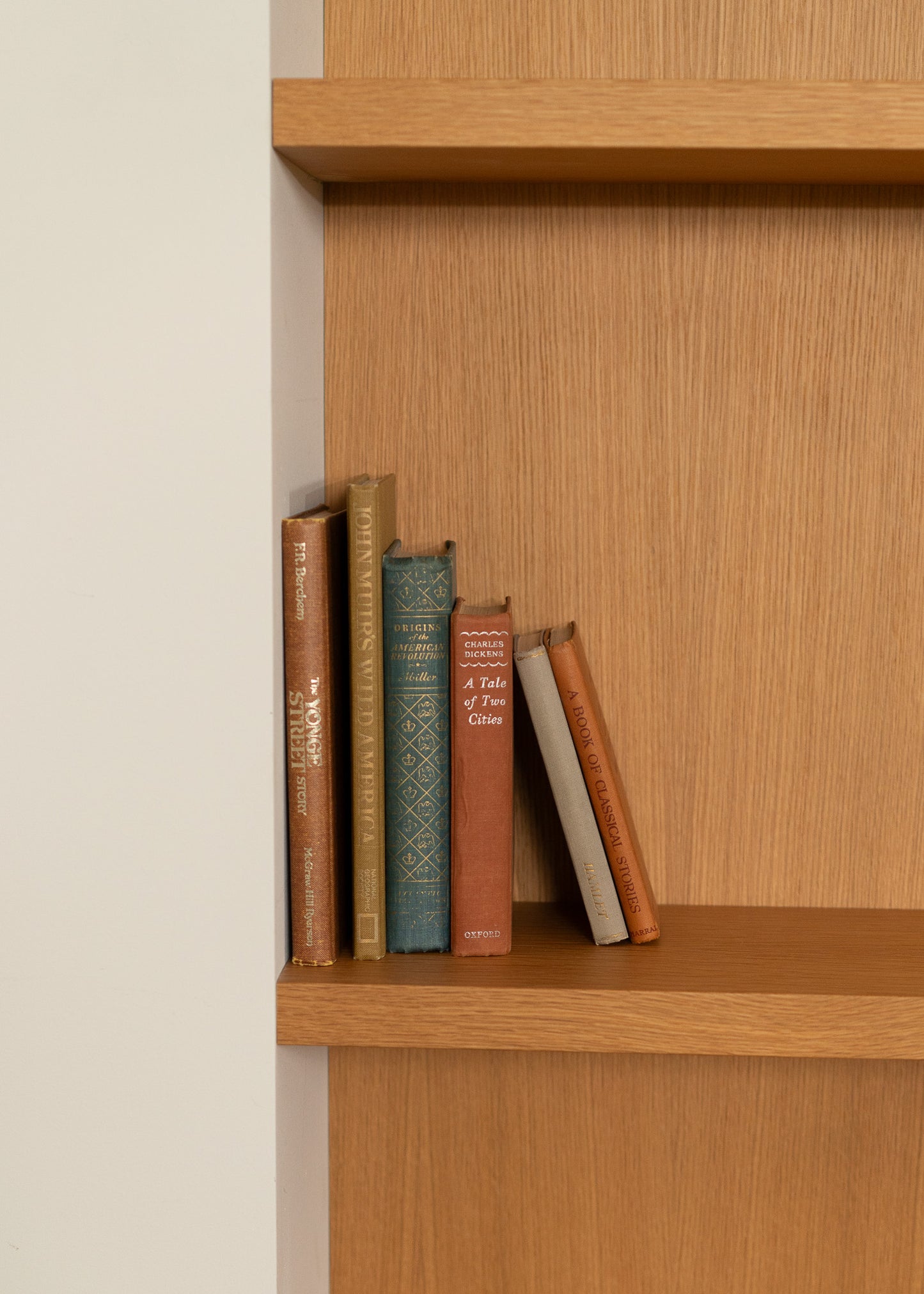 Wooden bookshelf with vintage books against a beige wall