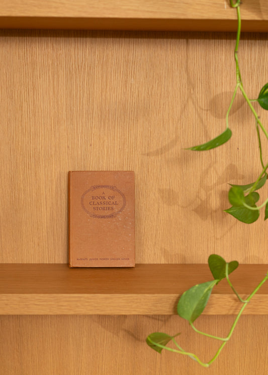 Brown vintage Greek classical stories book on a wooden shelf with a plant in the foreground