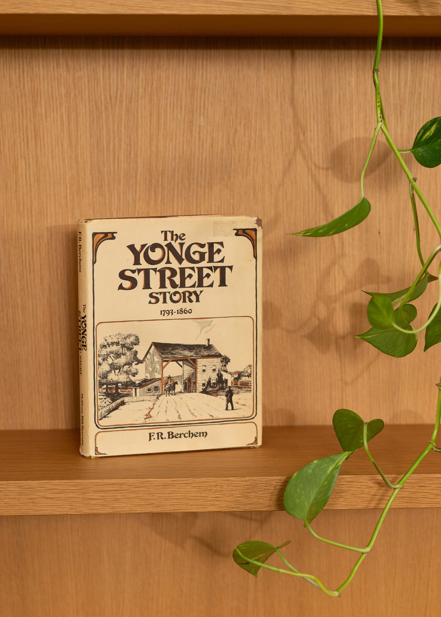 Vintage book titled 'The Yonge Street Story' by F.R. Berchem on a wooden shelf with a plant.