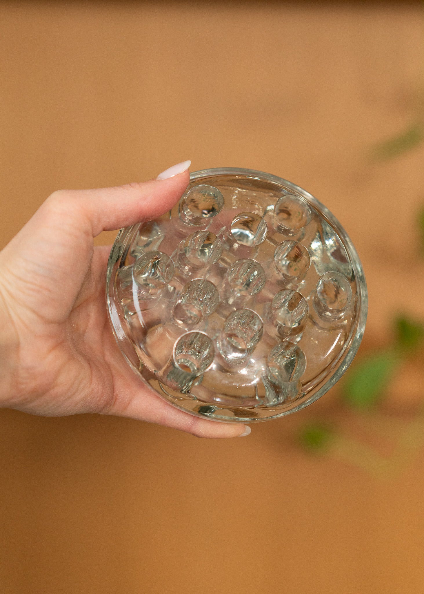 Hand holding a vintage round, clear glass flower frog against a blurred background