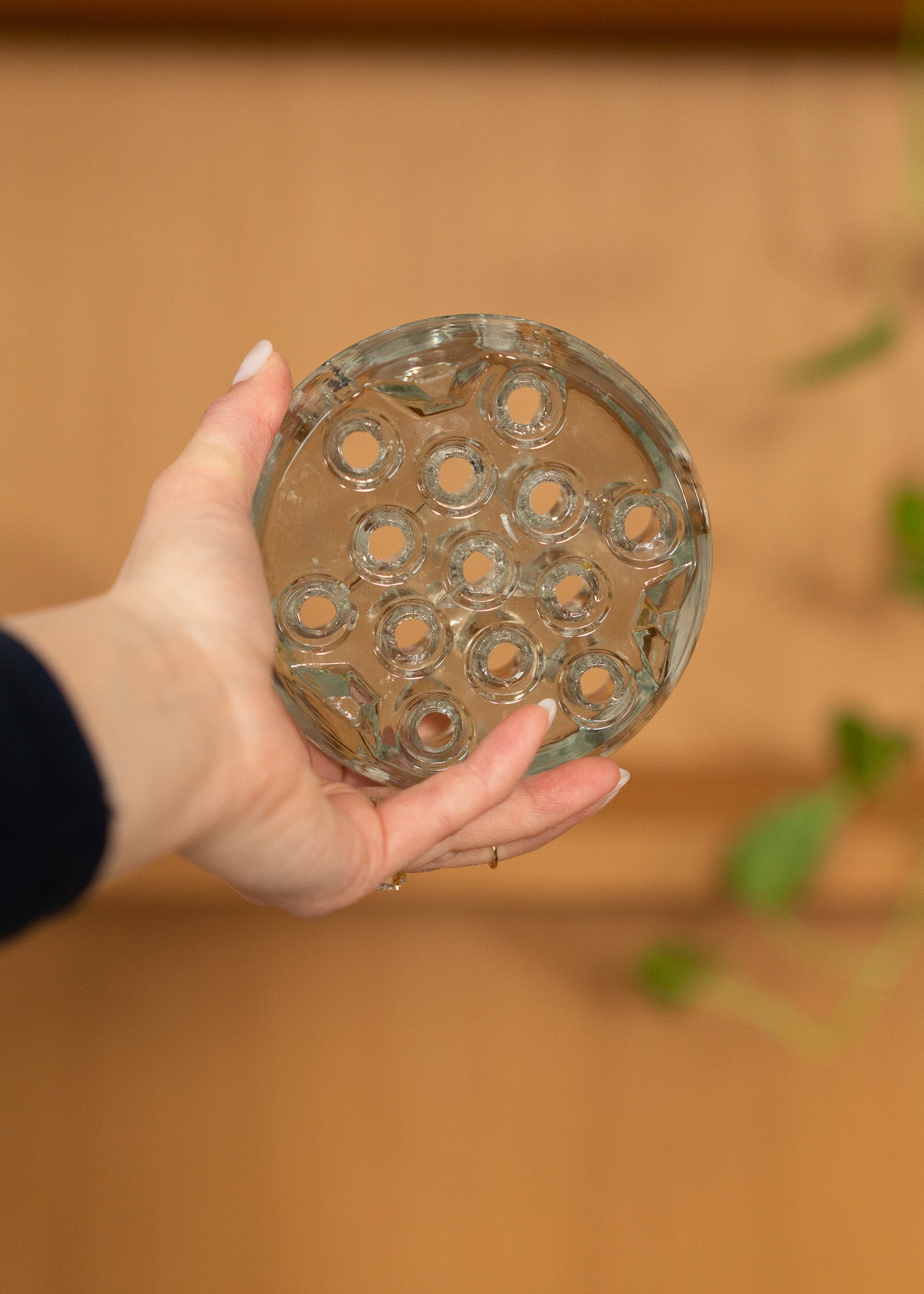 Hand holding a vintage round, clear glass flower frog against a blurred background