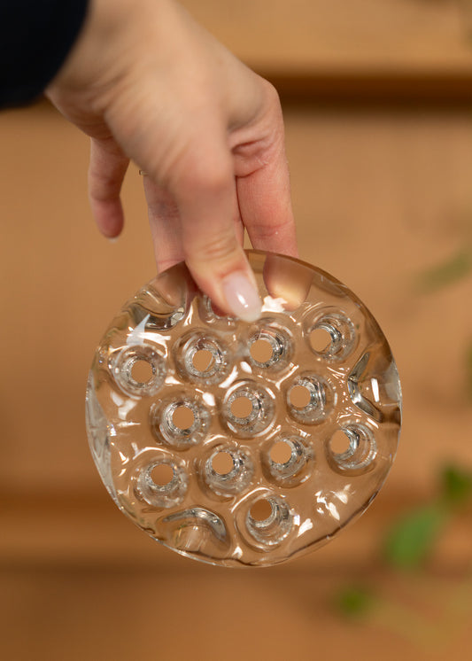 Hand holding a vintage round, clear glass flower frog against a blurred background