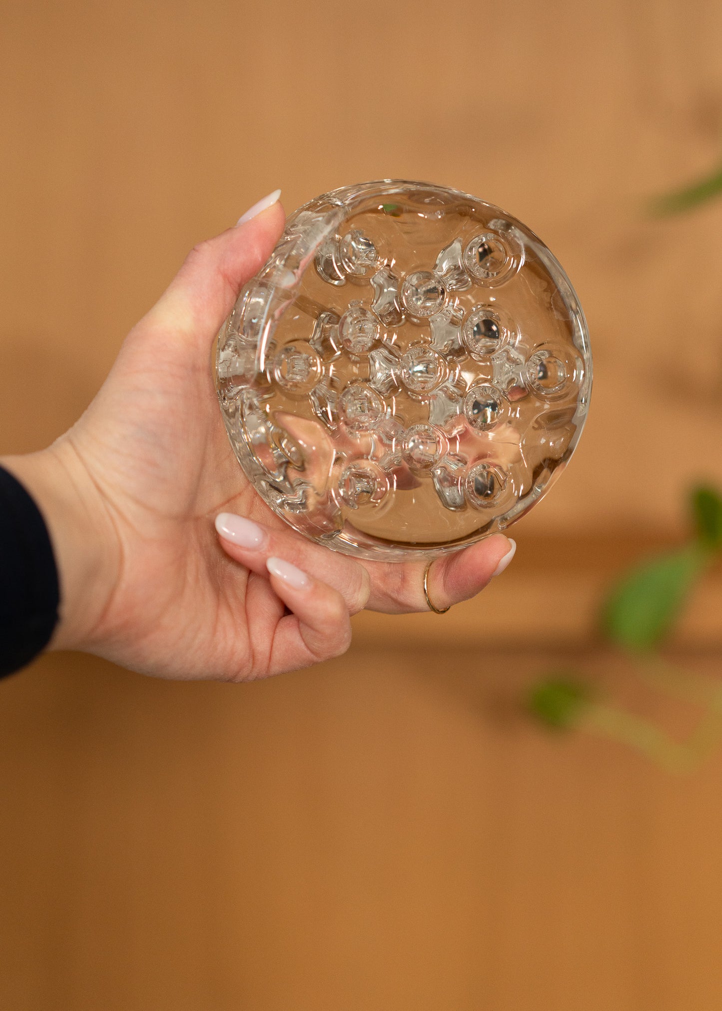 Hand holding a vintage round, clear glass flower frog against a blurred background