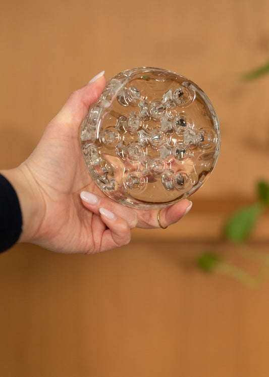 Hand holding a vintage round, clear glass flower frog against a blurred background