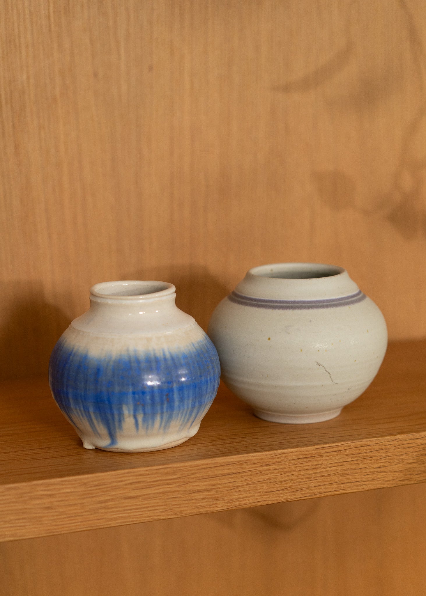 Two vintage ceramic jars with blue and white glaze on a wooden shelf.