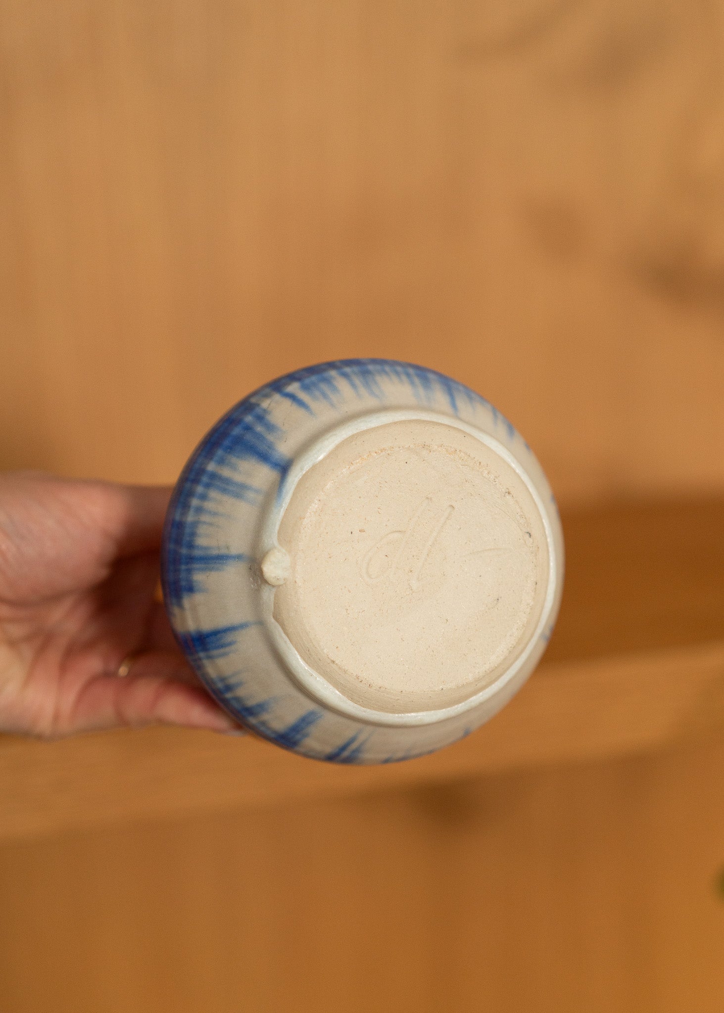 Ceramic container with blue and white design held by a hand on a wooden surface