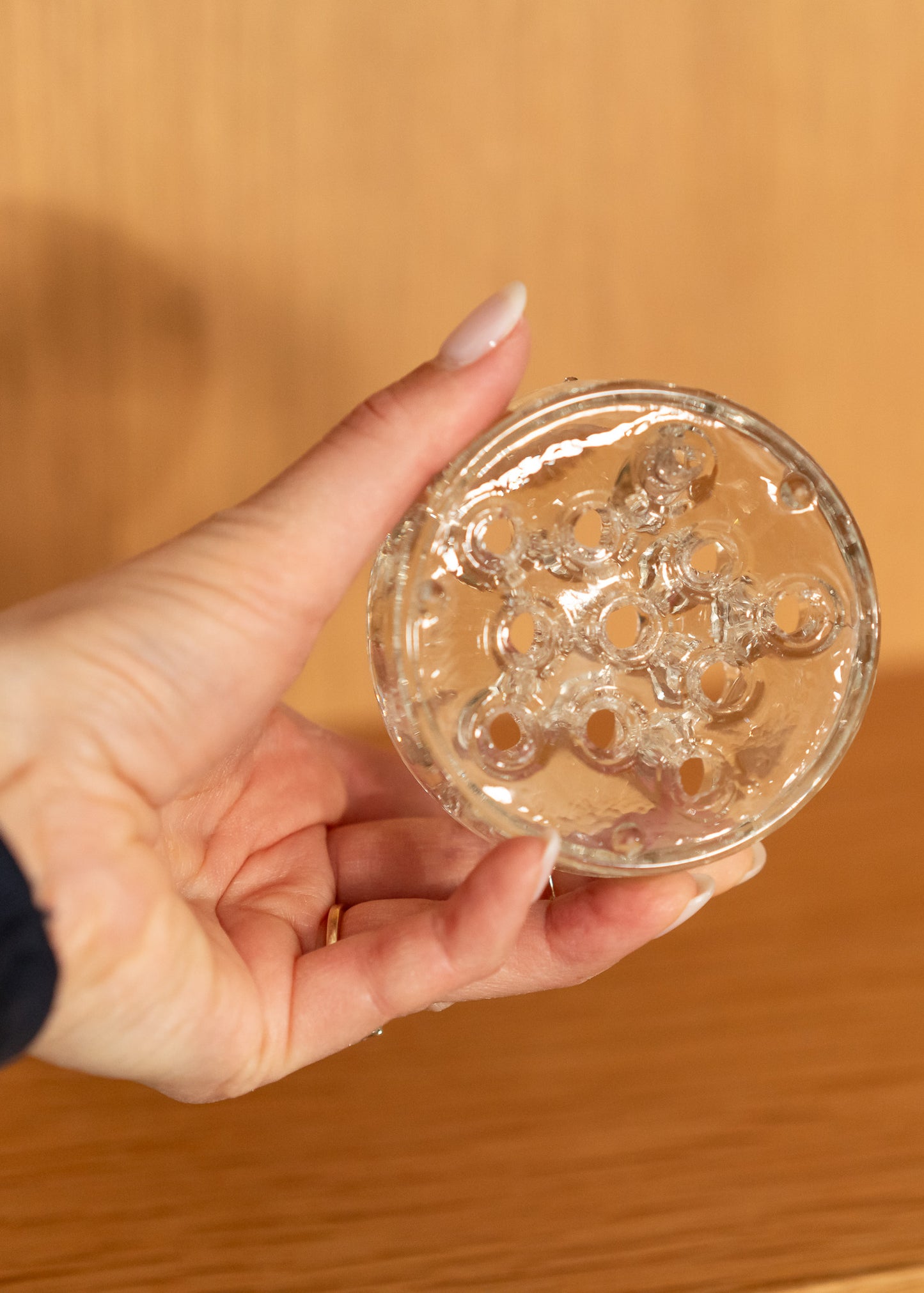 Hand holding a vintage round, clear glass flower frog against a blurred background