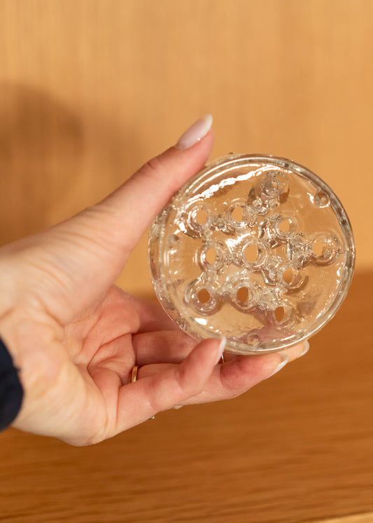 Hand holding a vintage round, clear glass flower frog against a blurred background