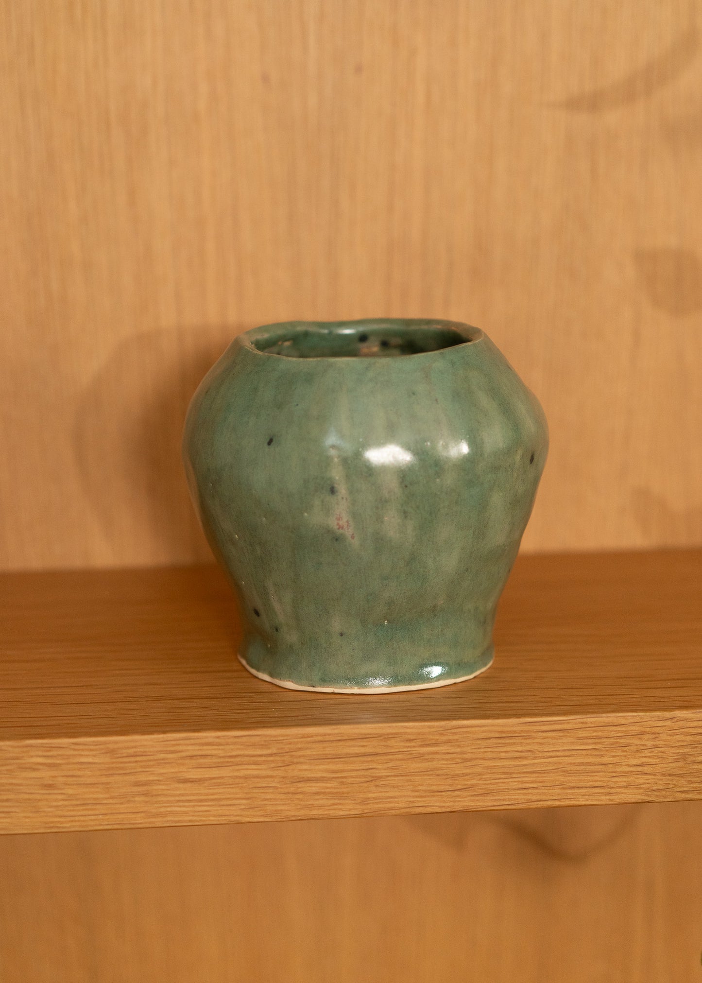 Green vintage ceramic vase on a wooden shelf with a wooden wall background