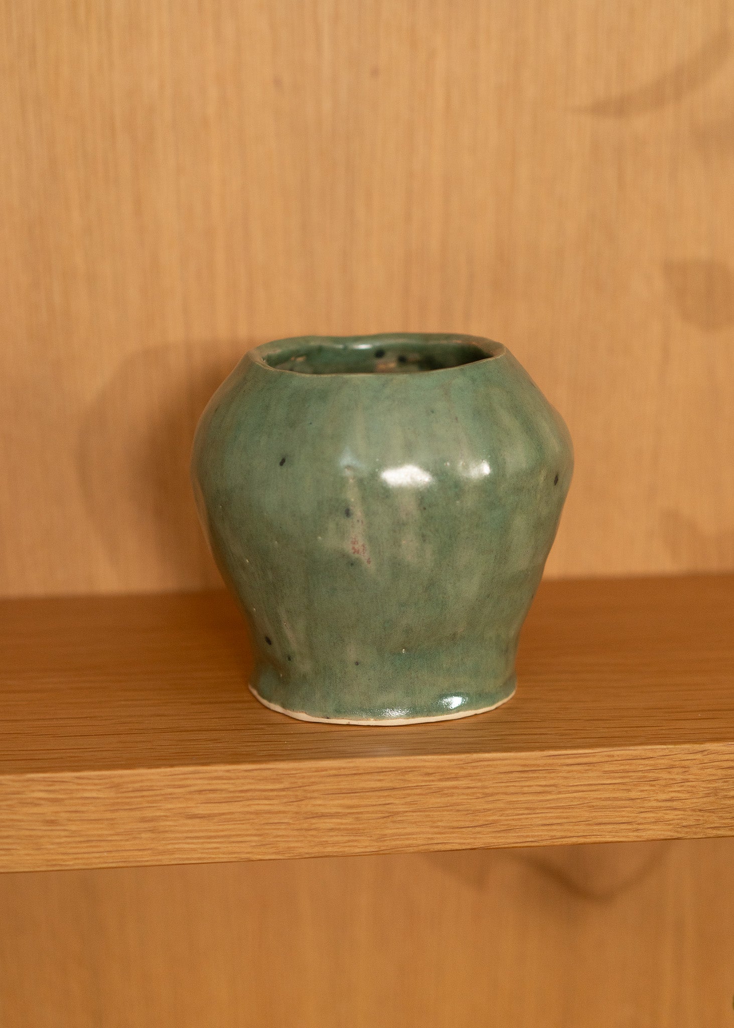 Green vintage ceramic vase on a wooden shelf with a wooden wall background