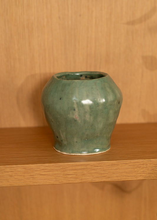Green vintage ceramic vase on a wooden shelf with a wooden wall background