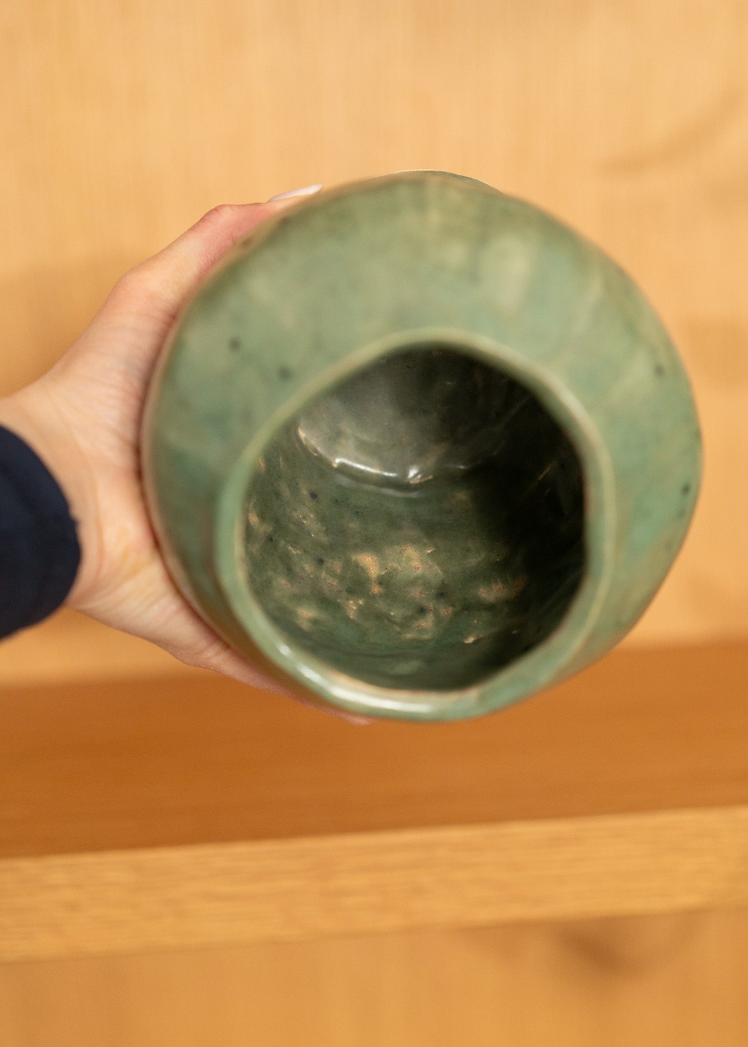 Hand holding a vintage green ceramic vase against a wooden background
