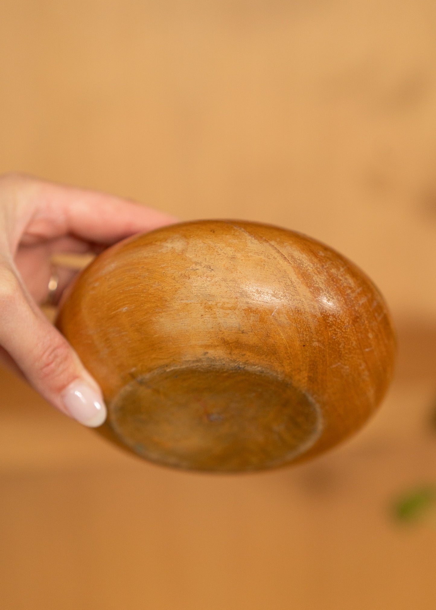 Hand holding a vintage wooden bowl against a blurred brown background