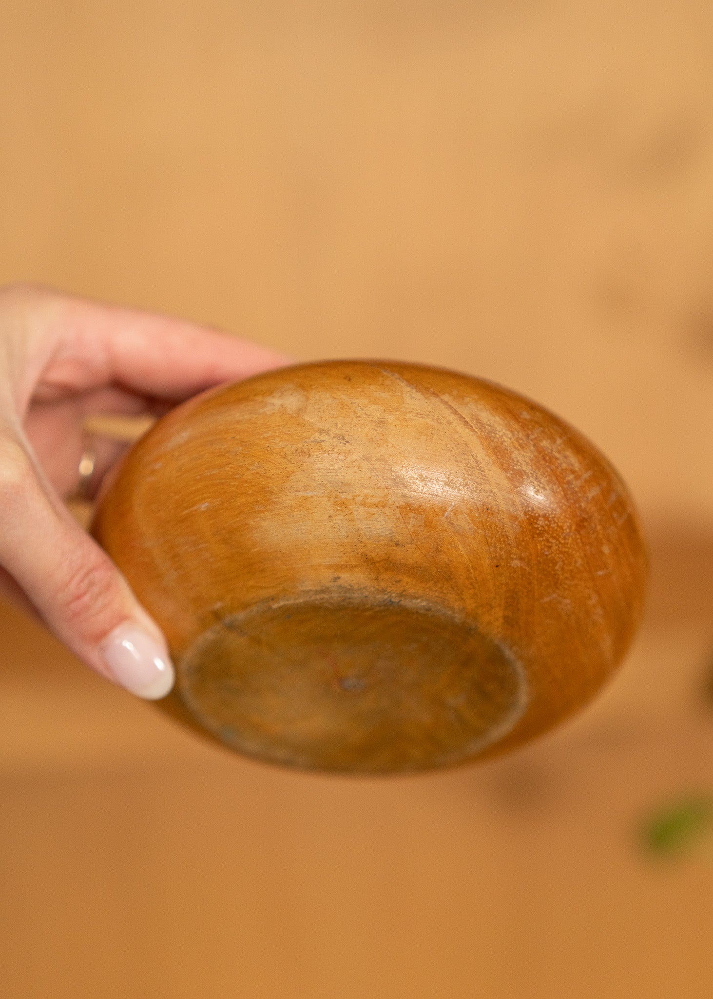 Hand holding a vintage wooden bowl against a blurred brown background