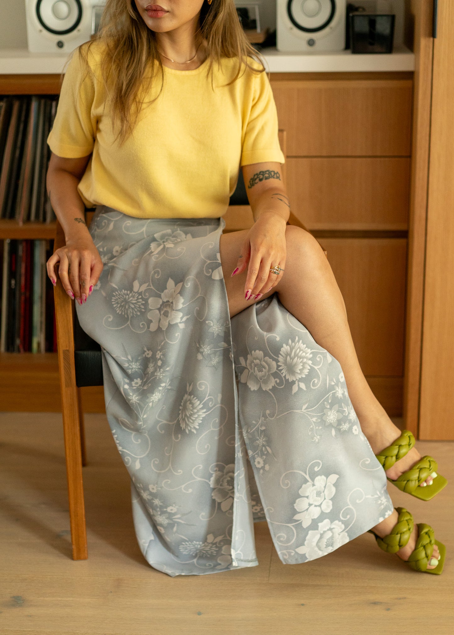 Person wearing a yellow top and vintage light grey floral skirt sitting on a wooden chair.