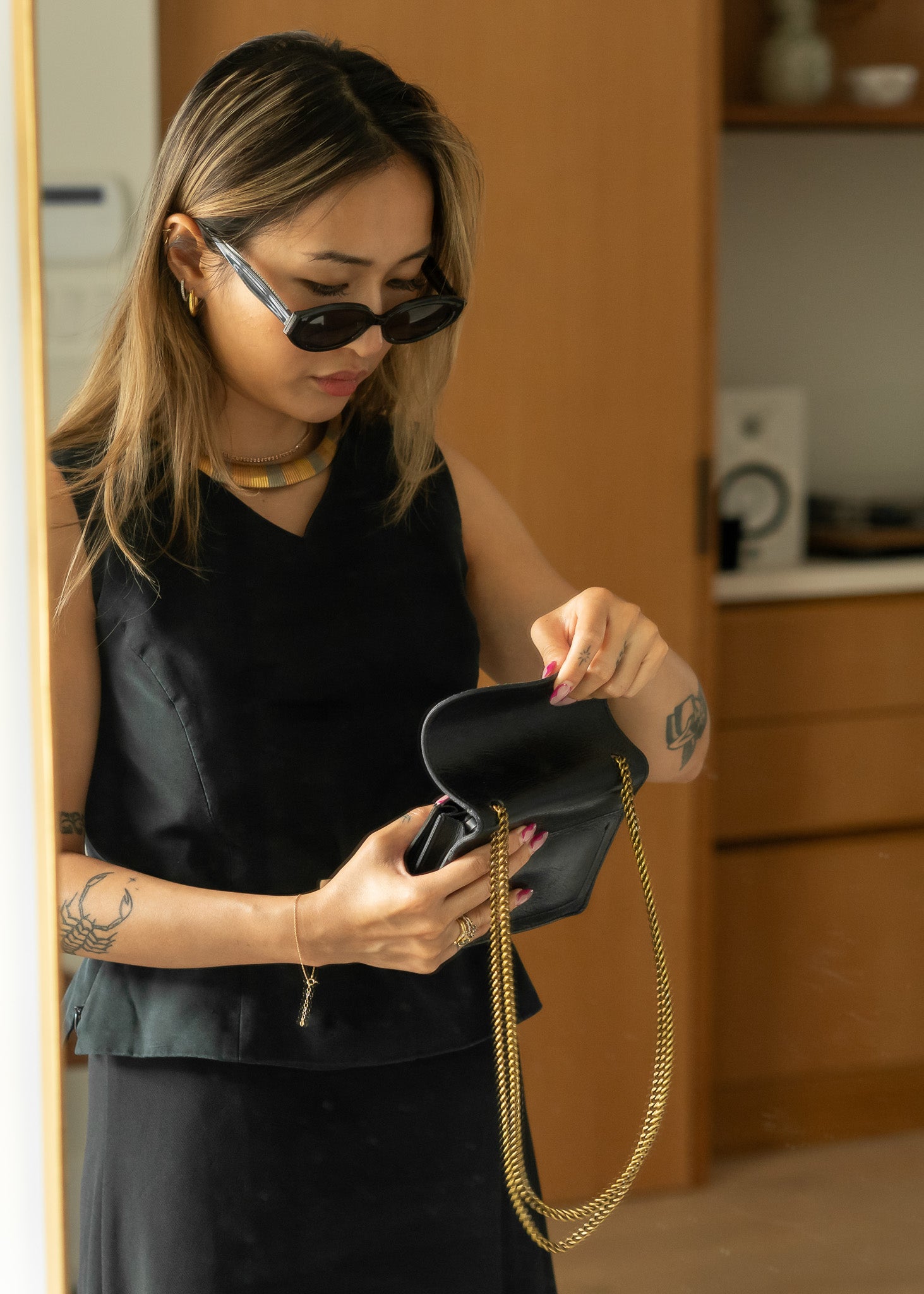 Woman wearing a metal necklace holding a black handbag with gold chain strap indoors.