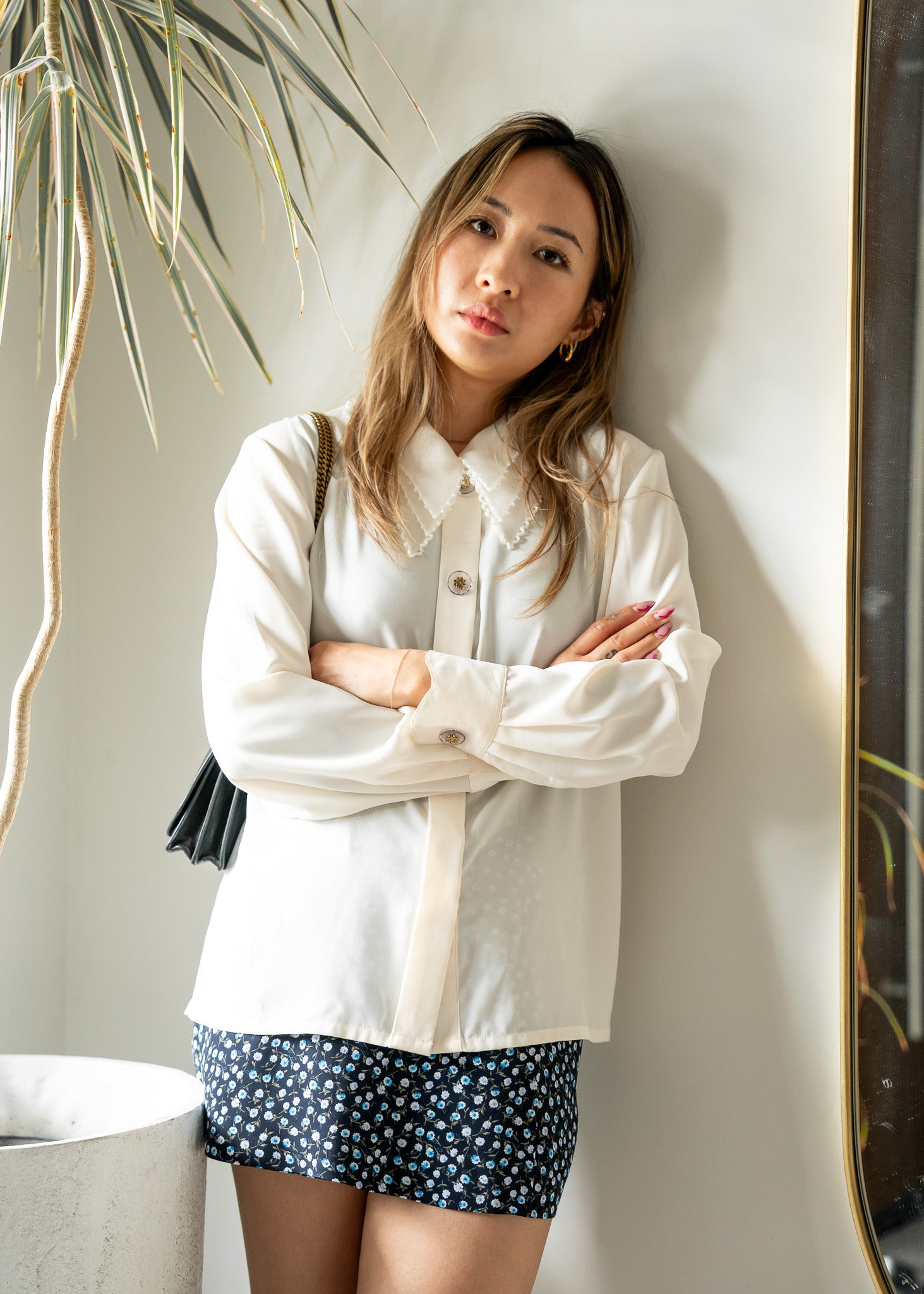 Woman wearing a white beaded blouse and navy floral skirt standing against a light wall.